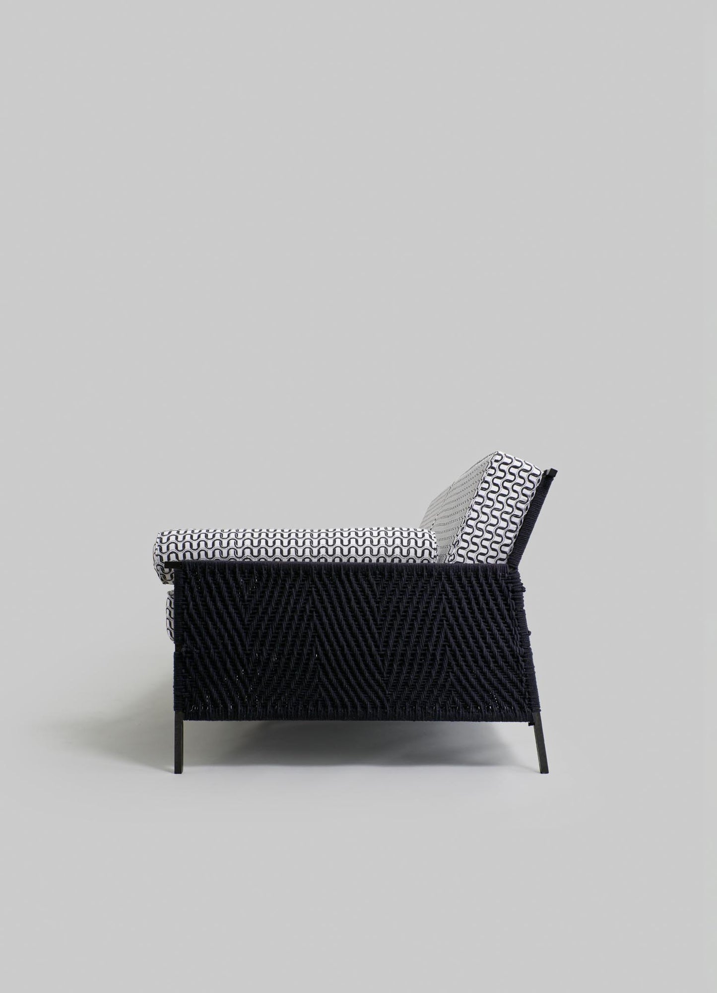 A modern armchair with a black woven base and a backrest, featuring a black-and-white geometric patterned upholstery on the seat and back cushion.