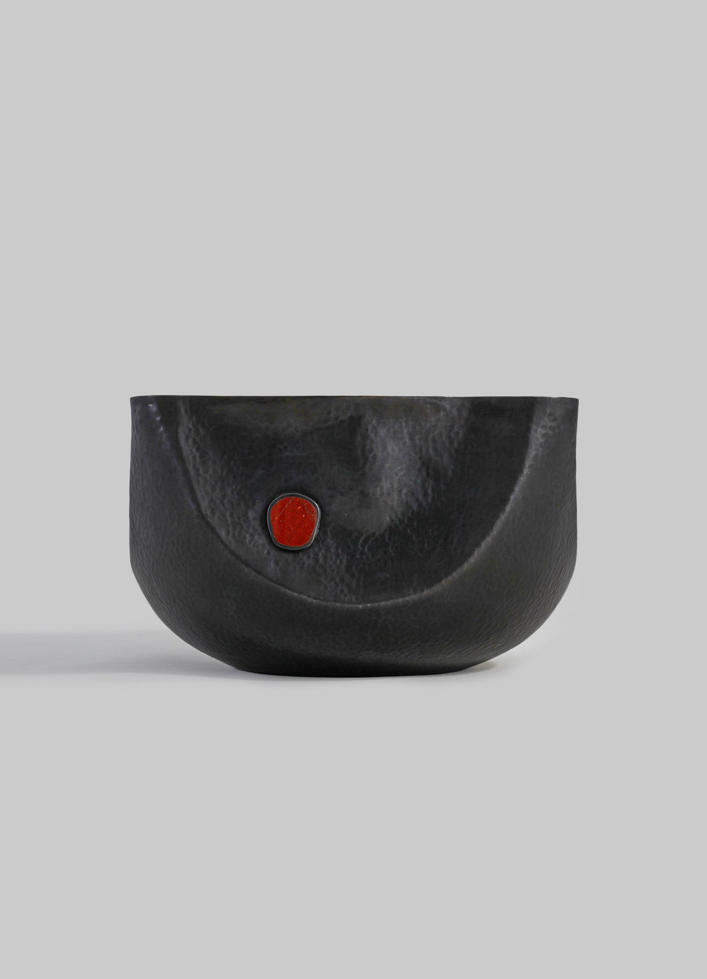 A black hammered leather bowl with a small red accent detail, featuring a smooth, rounded shape on a neutral background.