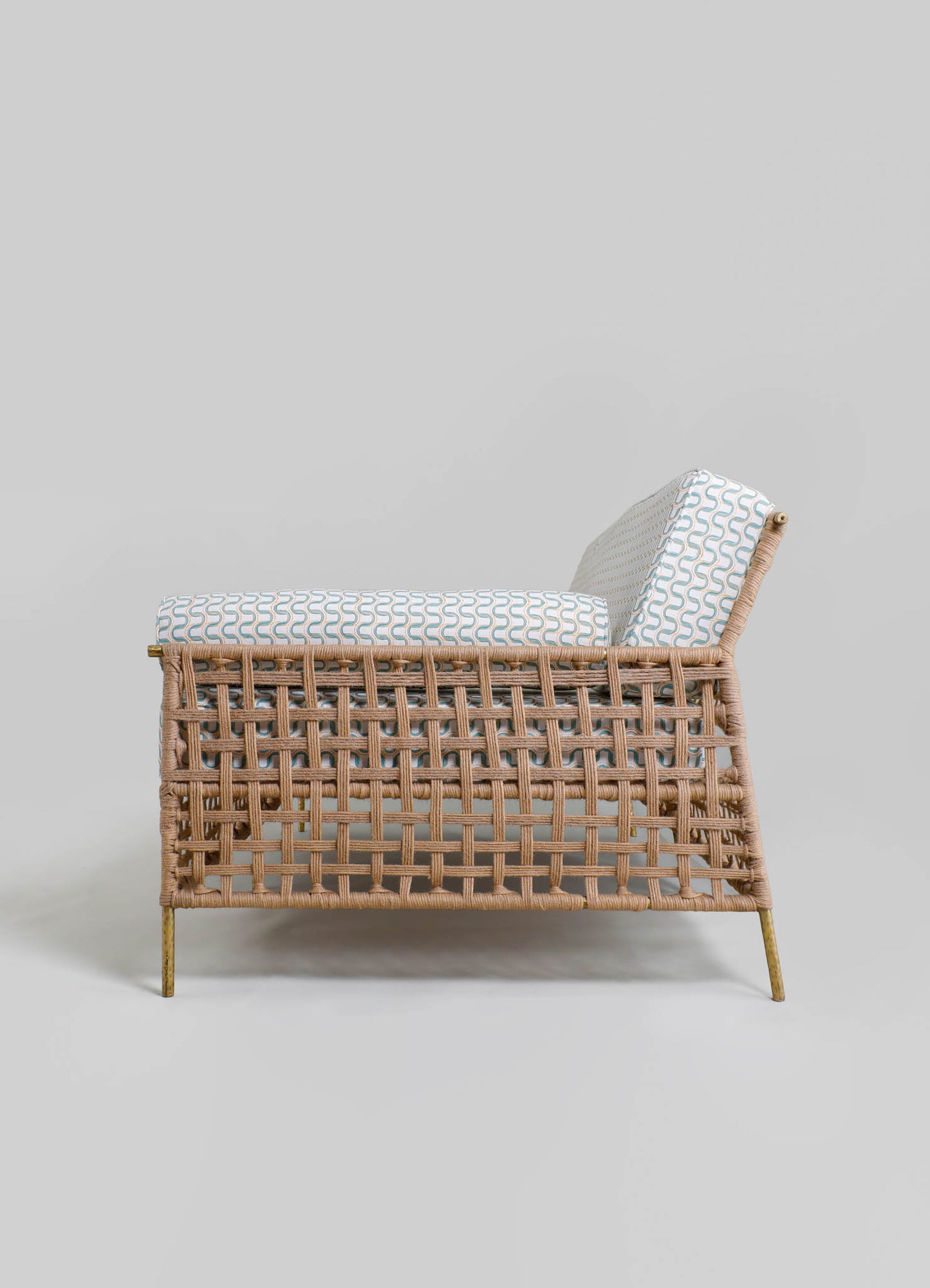 A rattan armchair with a woven lattice design, featuring a light beige finish and slim metal legs, topped with a cushioned seat and backrest with a geometric pattern in soft blue and white.