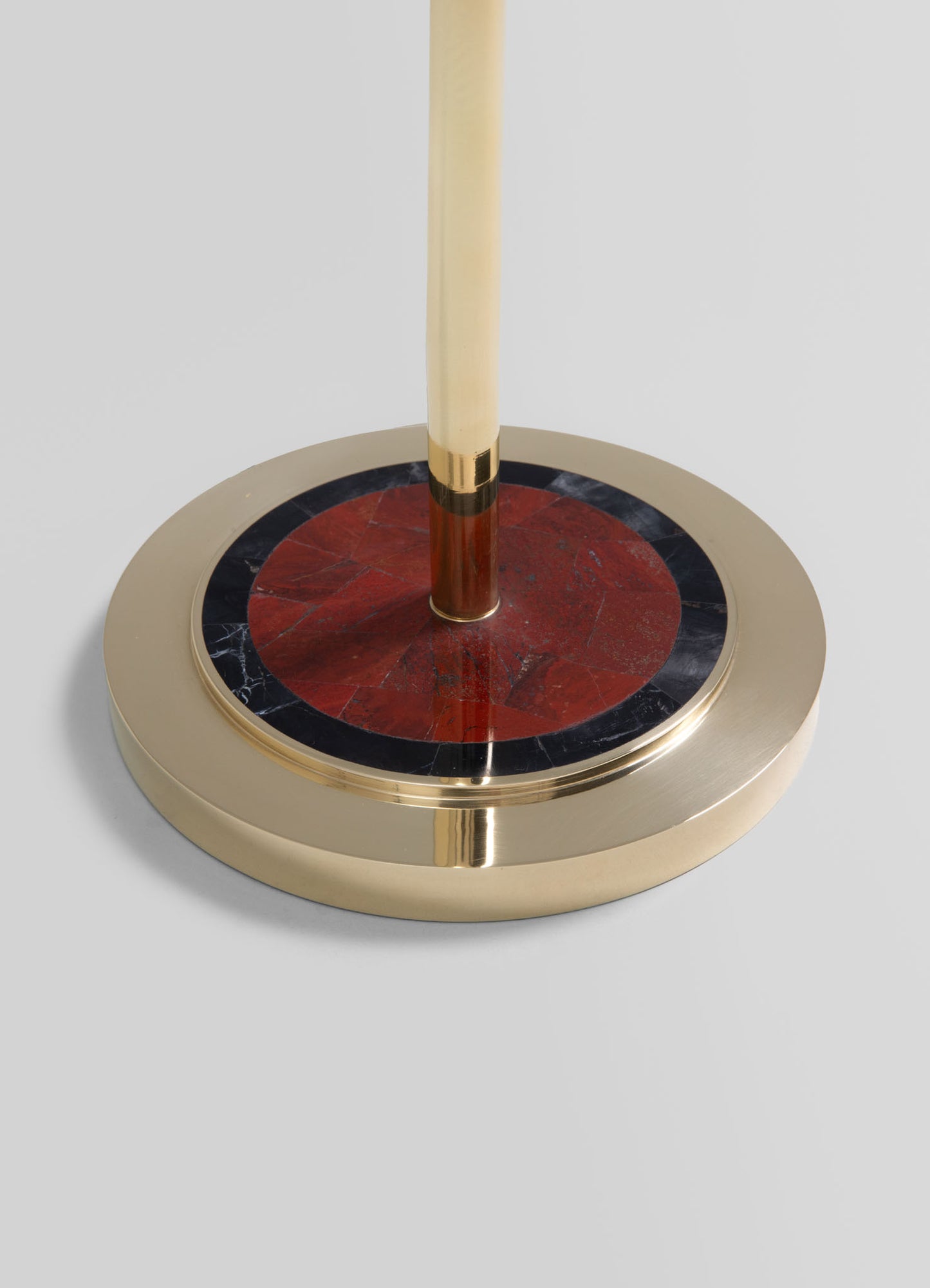 A decorative table base featuring a circular metal frame with a gold finish, a central red-marble disc, and black marble accents around the marble. The design combines contemporary materials with bold color contrasts.