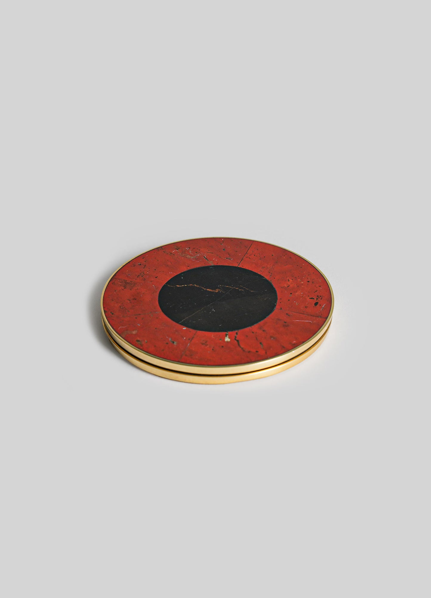 A round coaster set with a black center and a red marble-patterned border, framed with a gold metal edge.
