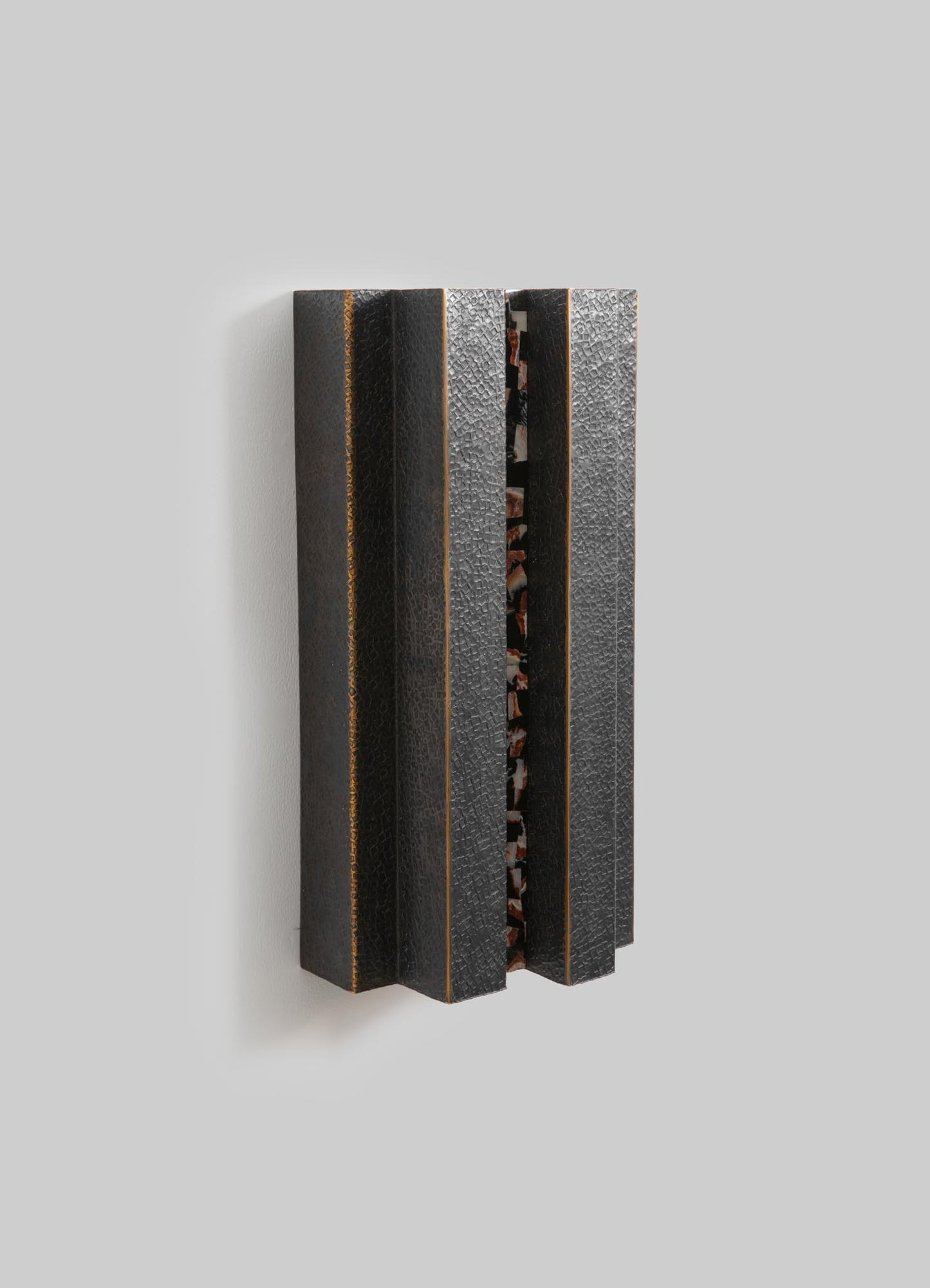 A modern wall-mounted sculpture with a textured black and brown leather finish, featuring vertical wooden slats with a central patterned inlay. The piece has a contemporary style with a tactile, layered design.