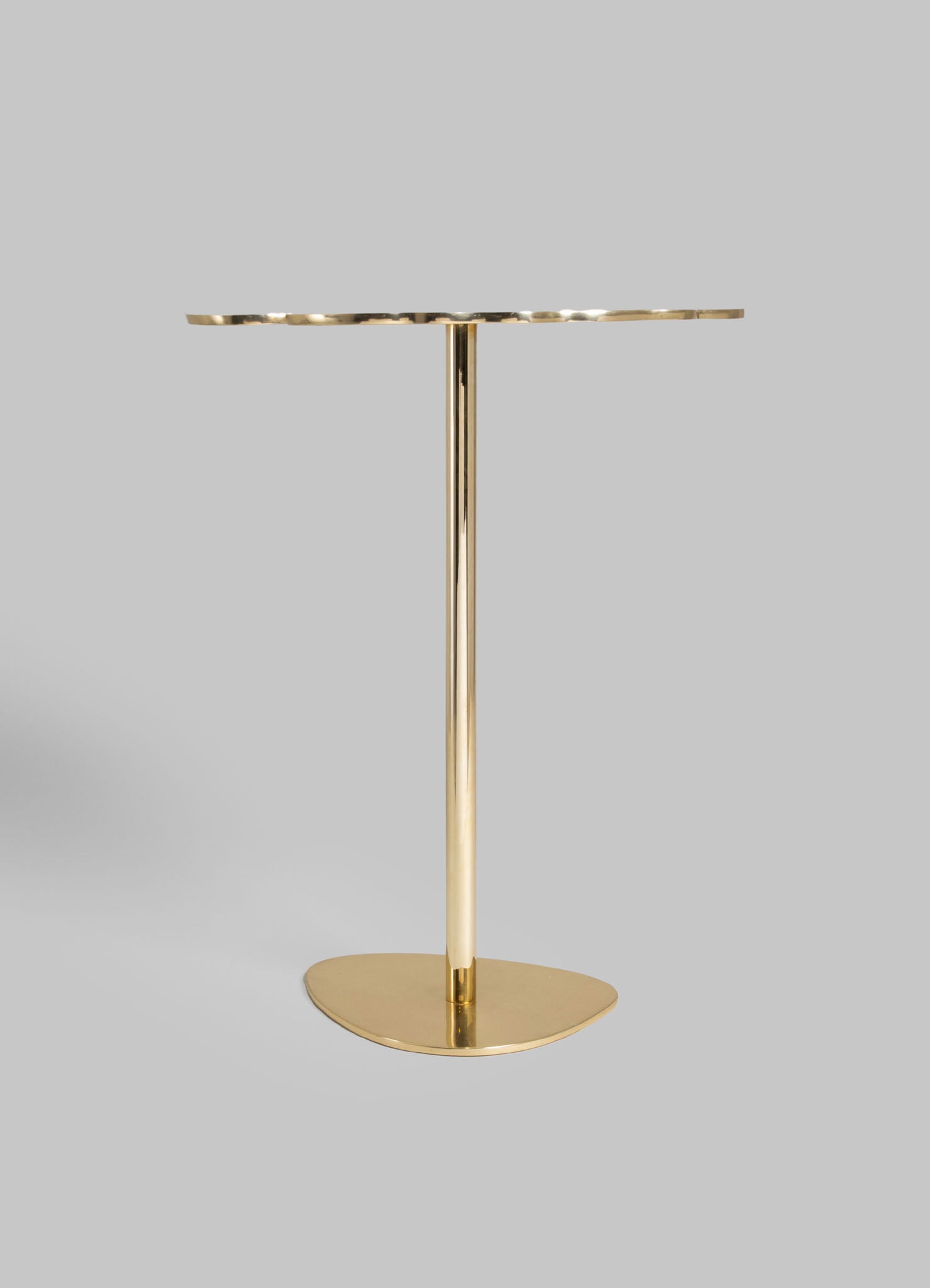 A modern gold-tone side table with a round, textured metal top and a slim, cylindrical pedestal base. The table features a minimalist design with a sleek, reflective finish, set against a plain gray background.