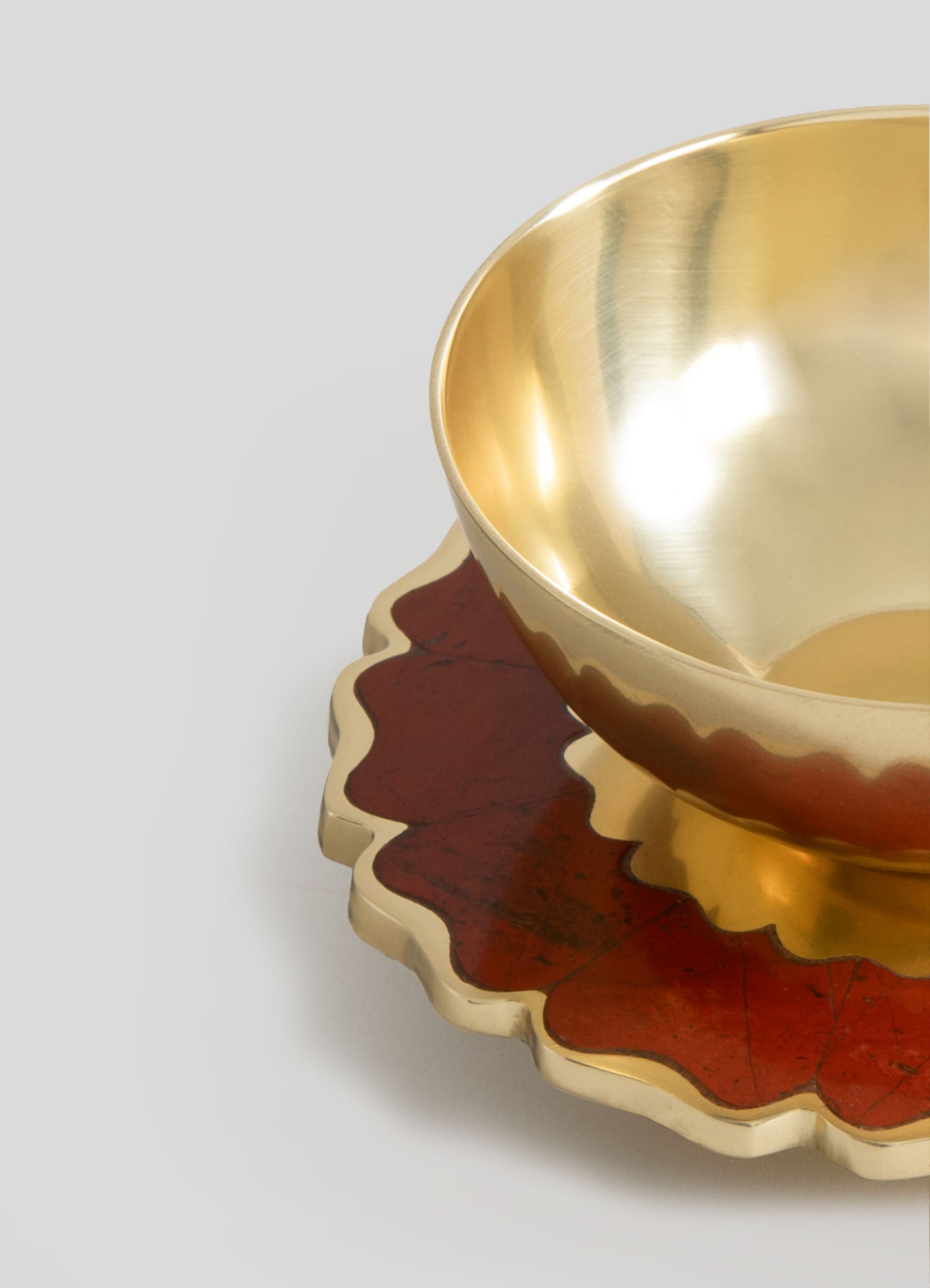 The image features a decorative brass bowl with a polished, reflective surface and a smooth, rounded shape, placed on a wooden tray with a scalloped edge and a reddish-brown finish.