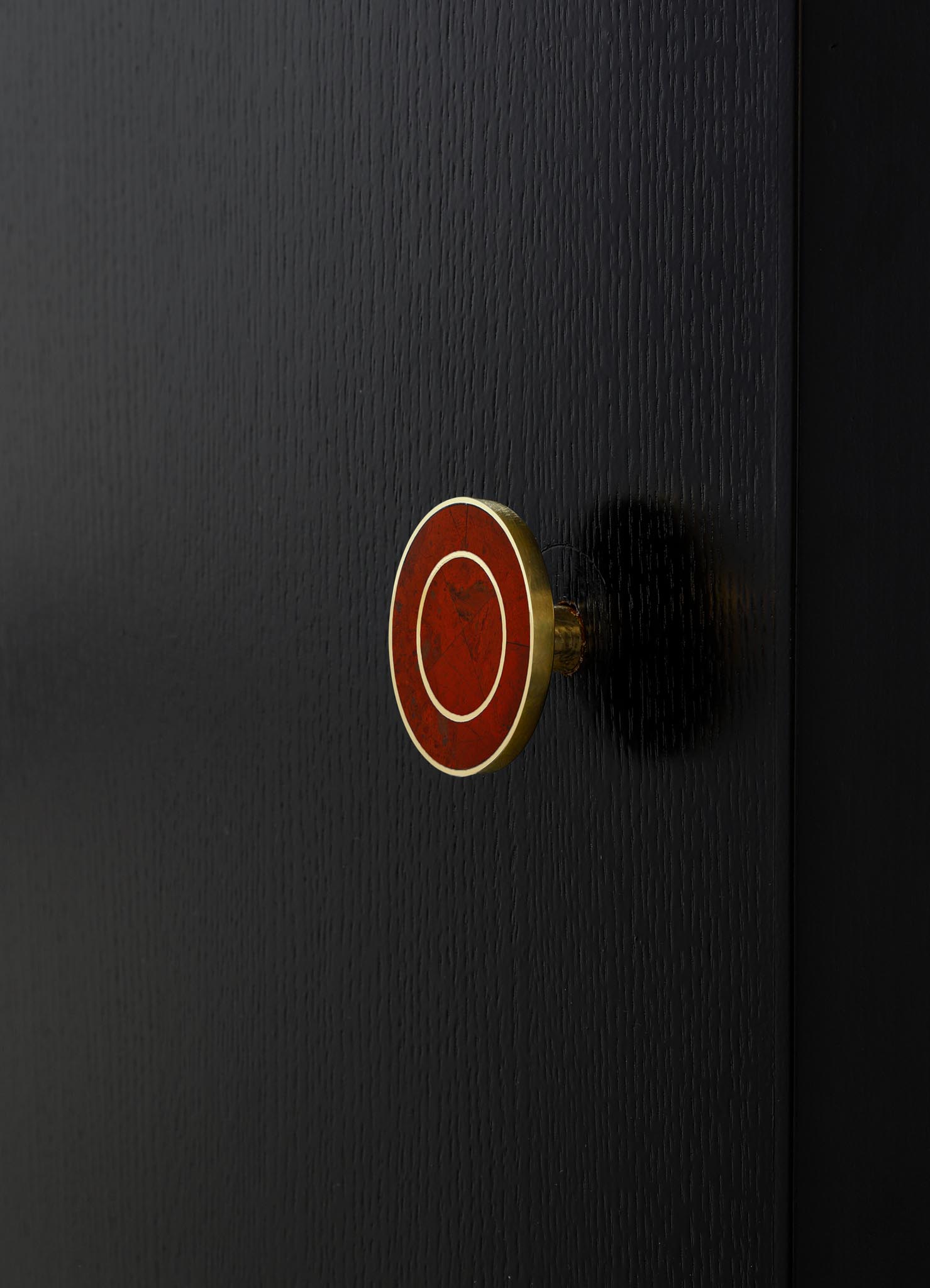 A close-up of a round, decorative wall element with a red, marbled pattern and gold border, mounted on a textured black surface.