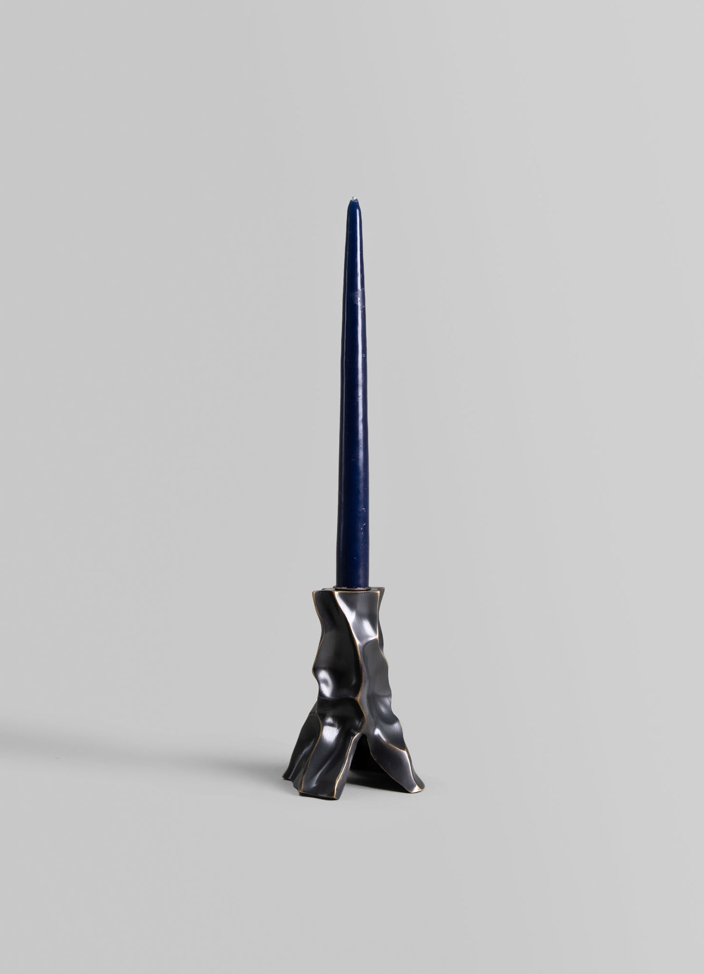 Ceramic candlestick holder with a textured, irregular black and metallic silver finish, designed to hold a tall, slender navy blue candle.