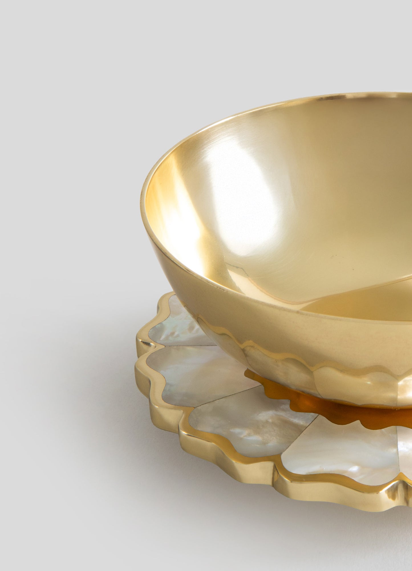 A set of two nested bowls with a shiny, metallic gold finish and smooth, rounded shapes, placed on a decorative scalloped-edged tray with a similar gold and pearl-like finish, creating a luxurious and elegant tableware presentation.