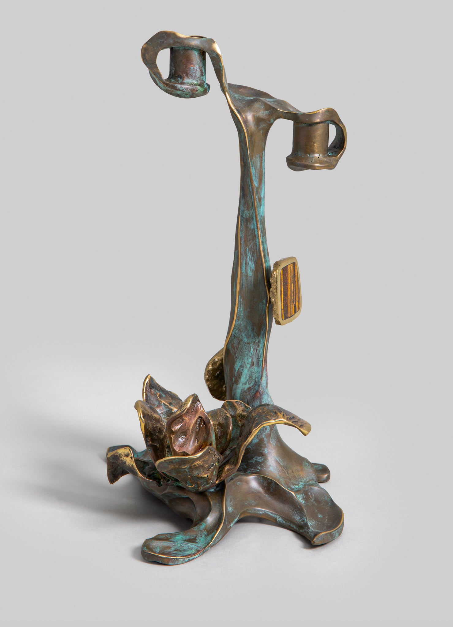 Bronze sculpture with an organic, floral motif featuring a tall, slender form and abstract, leaf-like base. The surface shows a patina with hints of green and gold accents, evoking a handcrafted and artistic style.