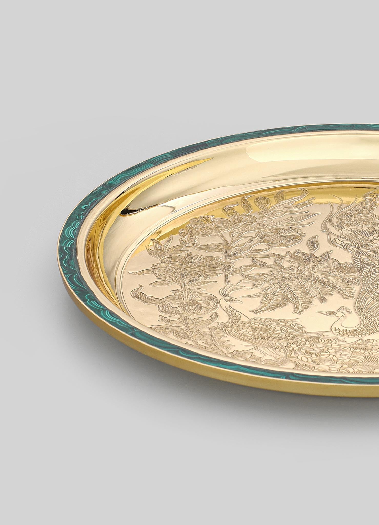 A decorative tray made of metal with a gold-tone finish, featuring engraved floral and peacock motifs and a border with turquoise and gold detailing.