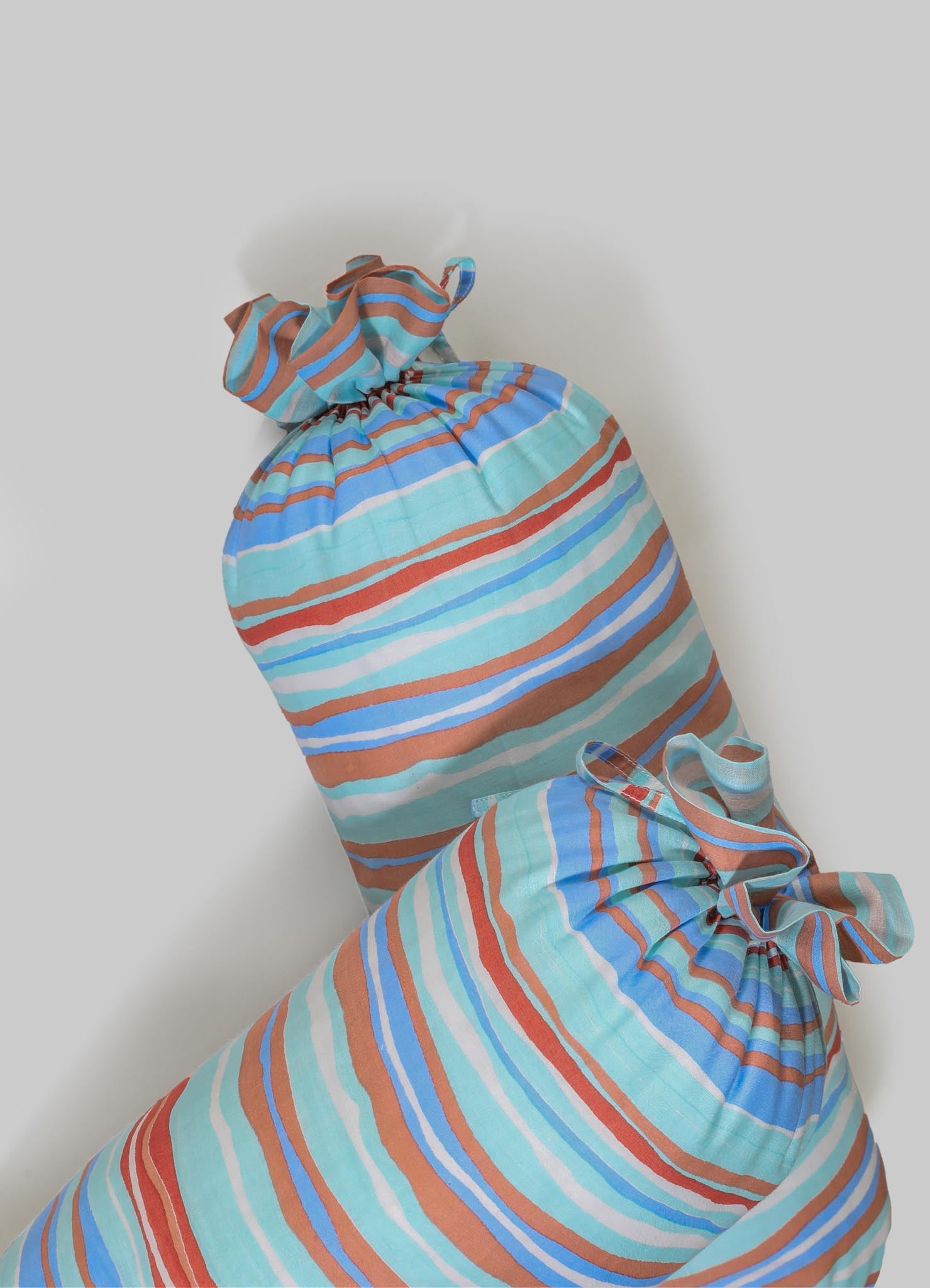 Striped fabric laundry bags made of lightweight cotton or similar material in pastel blue, rust, and tan colors, featuring drawstring closures and ruffled tops.