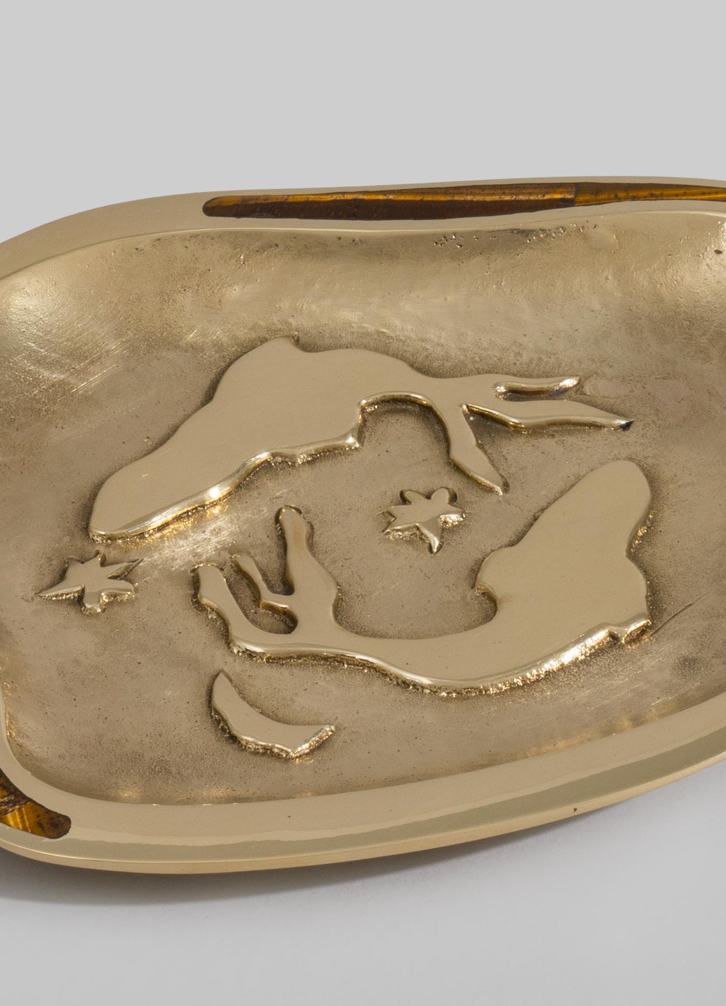Gold-toned metal tray with a raised floral motif in relief, featuring a smooth, polished surface and rounded edges, set against a plain background.