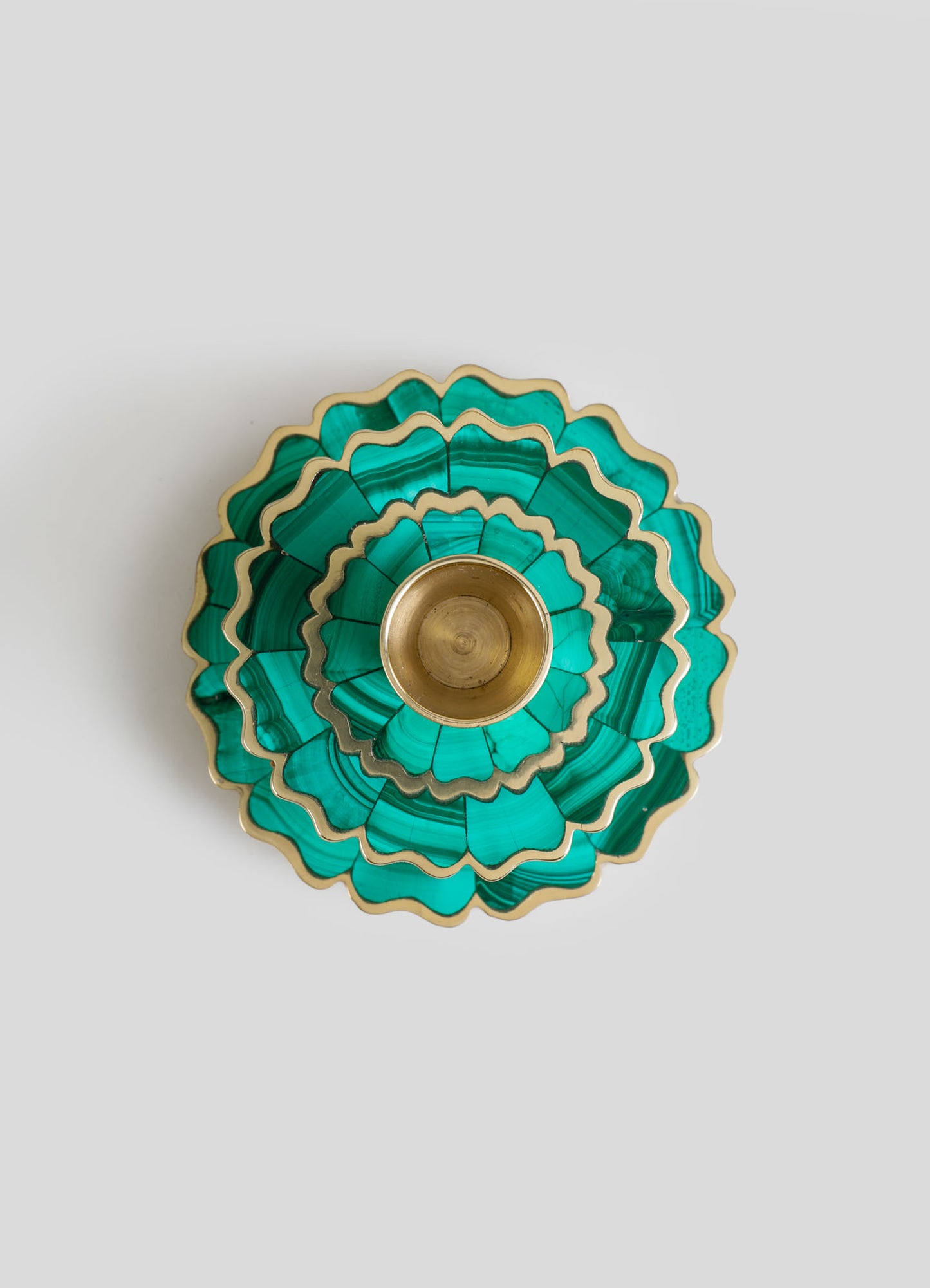 A layered decorative tray or tray with scalloped edges, made of malachite or a similar green stone with natural banding patterns, accented with gold trim. The tray features a brass or gold-colored central holder or cup.