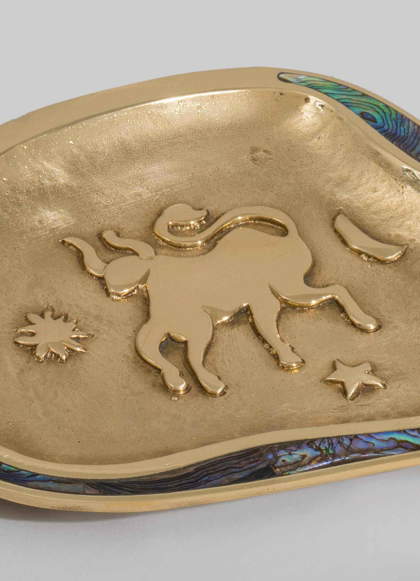 A decorative dish or tray made of metal with a gold finish, featuring embossed motifs of an elephant, a star, and a sun. The edges are adorned with abalone shell accents, adding an iridescent touch to the overall design.
