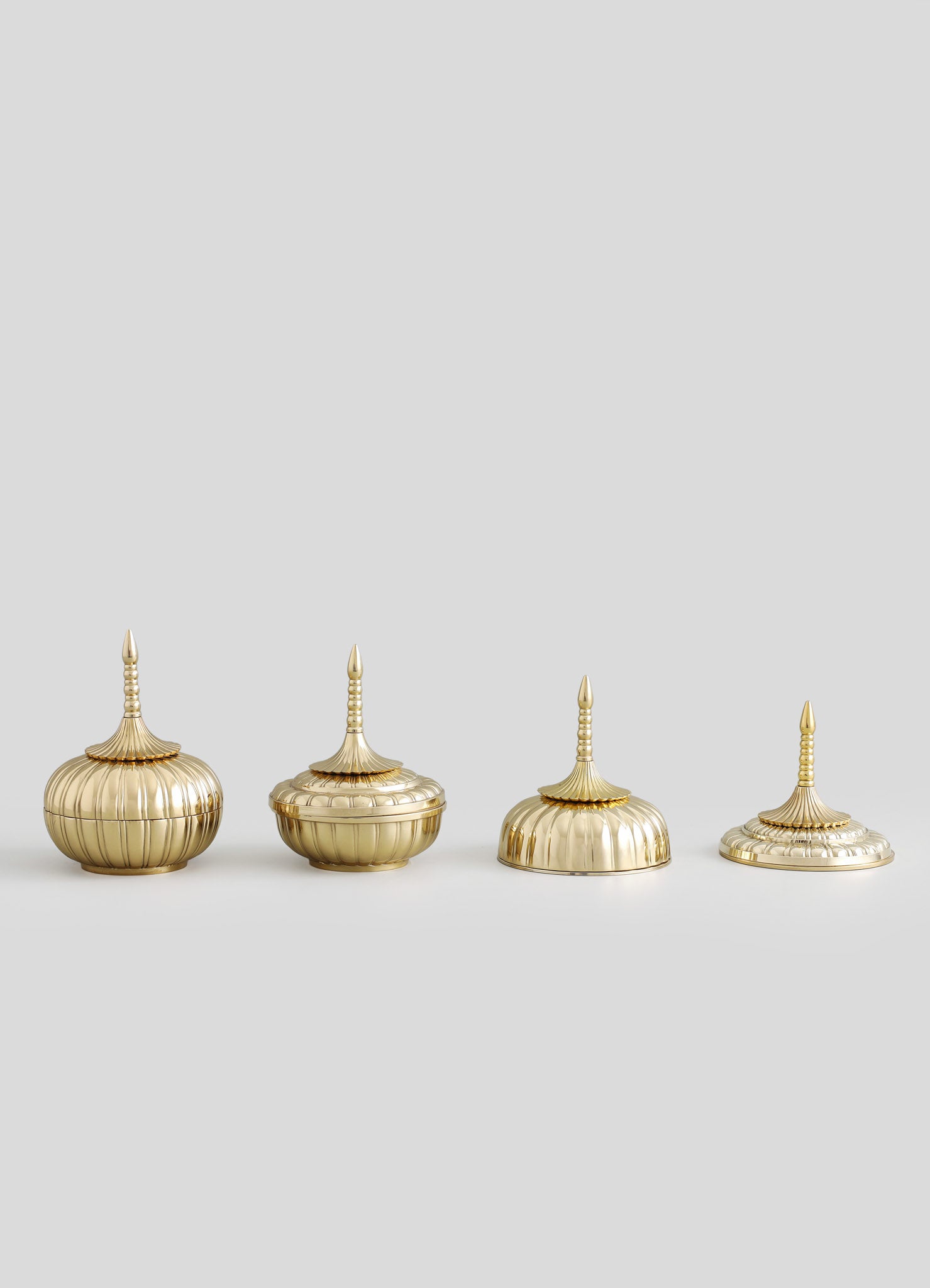 Four brass finial ornaments with ribbed, rounded bodies and tall, slender, pointed tops, featuring a shiny metallic finish and intricate carved details.