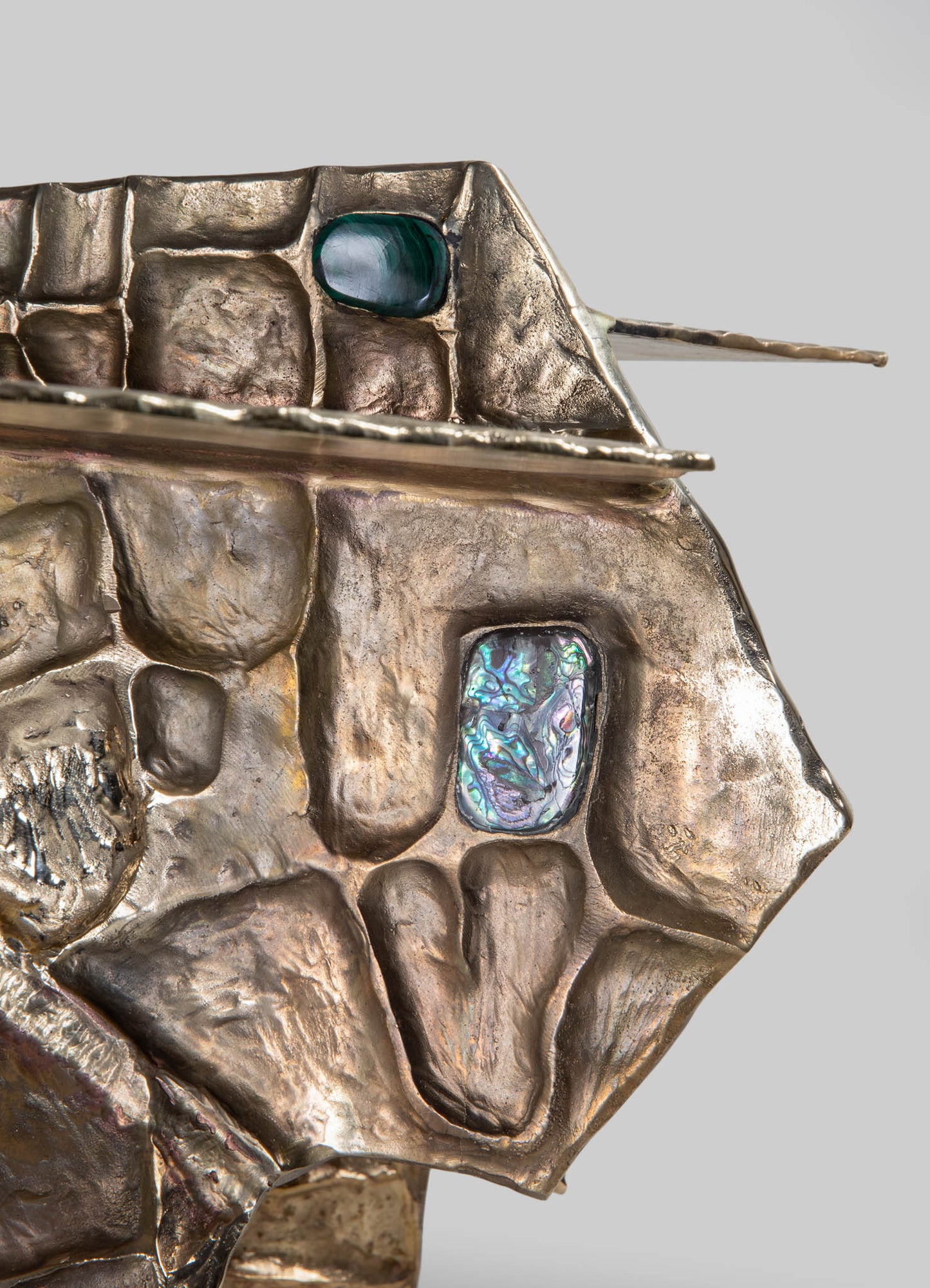 Object sculpture resembling an animal, crafted from textured metallic material with iridescent and smooth inlays, featuring a combination of rough and polished surfaces. The piece displays neutral metallic tones with colorful accents, emphasizing abstract and artistic design.