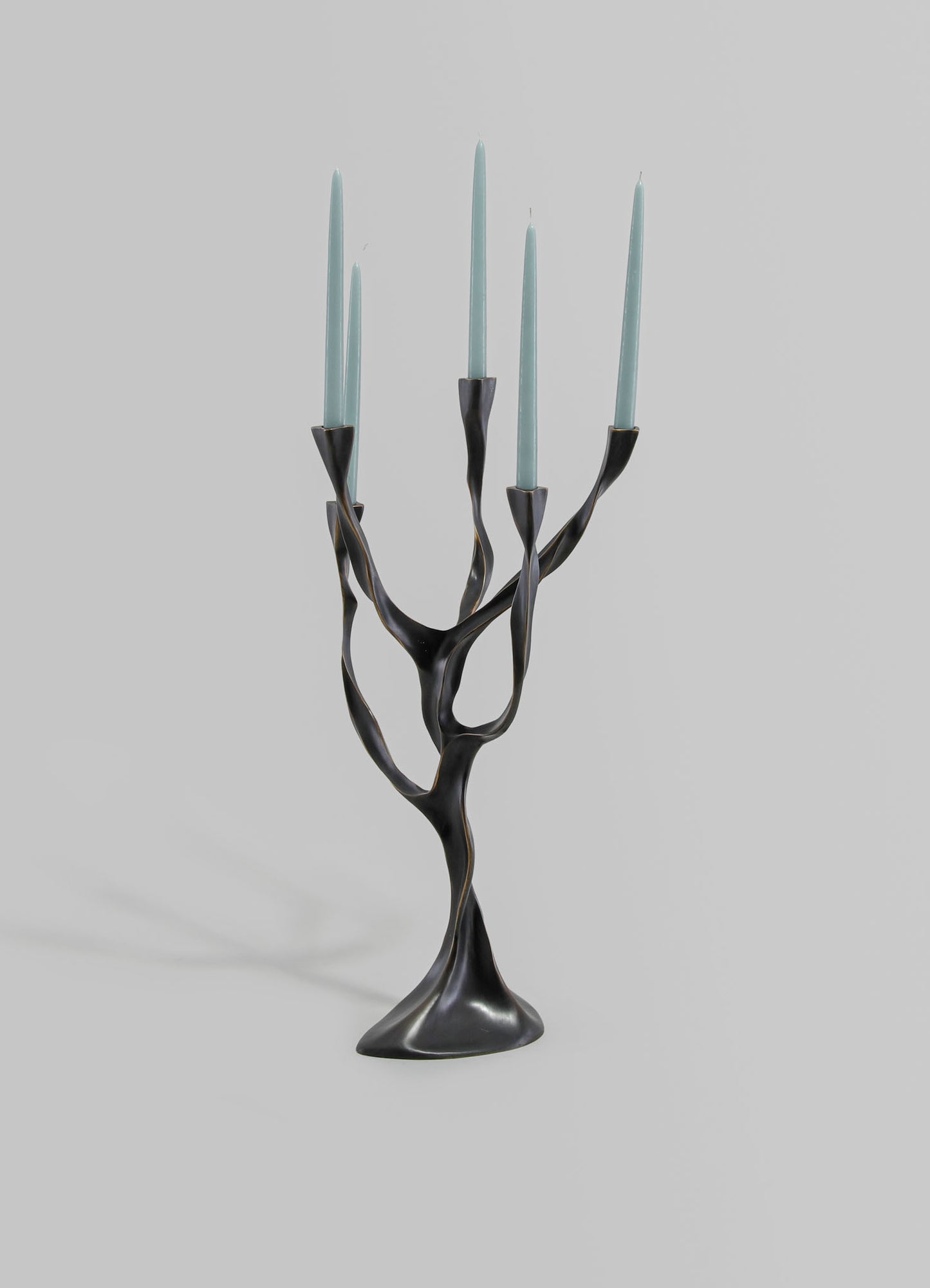 A modern black metal candelabrum with a twisted, branch-like design, holding five light blue tapered candles.