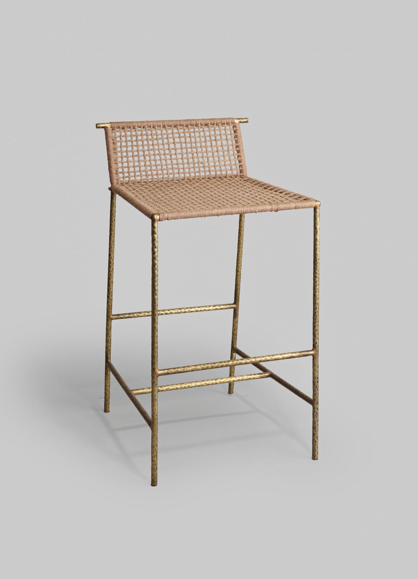 A bar stool with a brass hammered finish frame and a woven rattan seat and backrest, combining rustic and contemporary design elements.