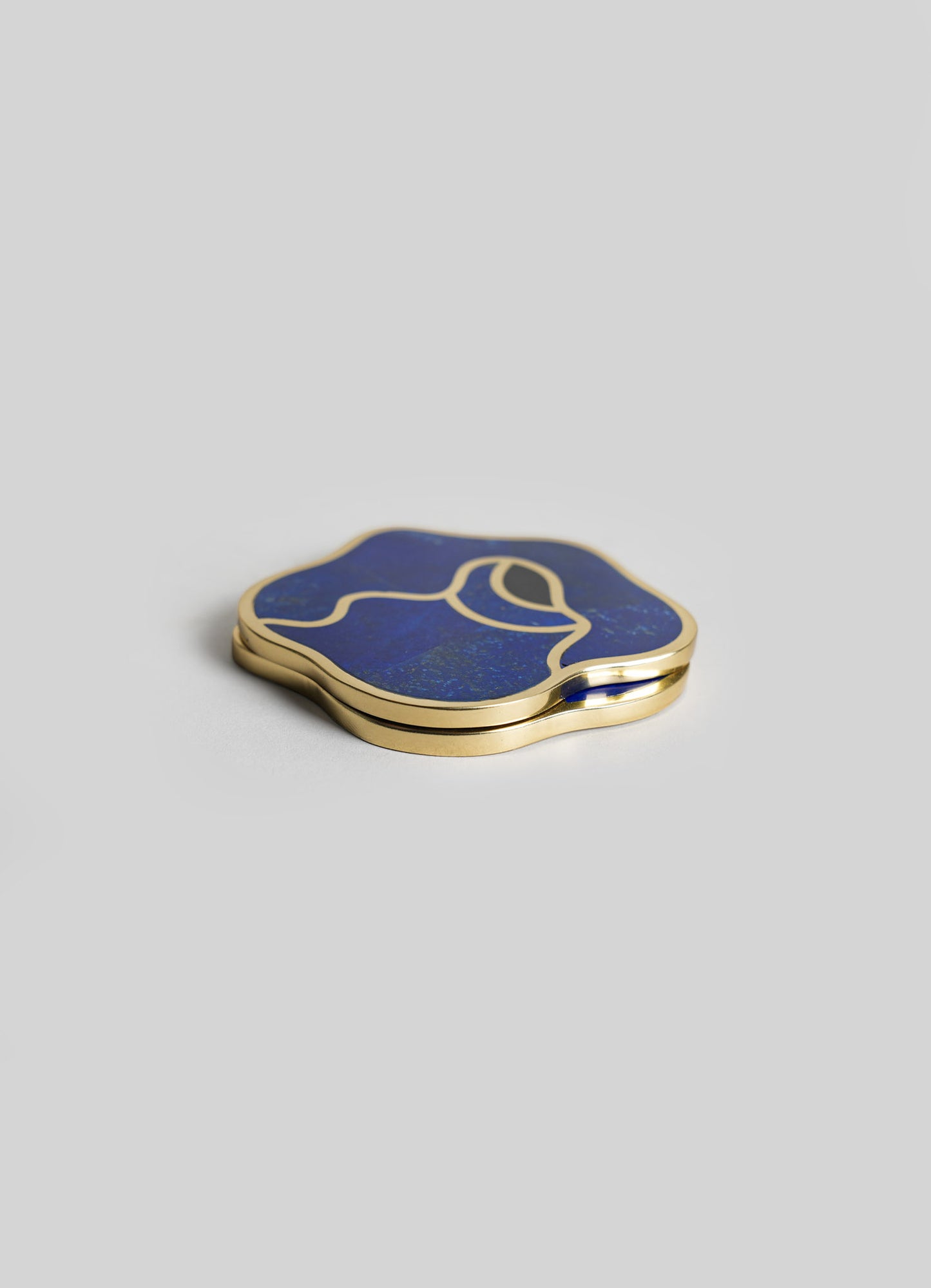 A decorative compact mirror with a floral-shaped design, featuring a brass frame and a deep blue inlay with gold accents. The mirror has an elegant, modern style with smooth, curved edges.