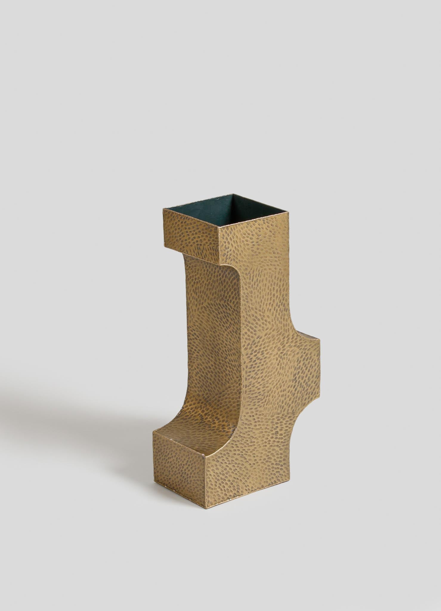 A decorative vase with a unique sculptural form in gold-toned metal, featuring a textured surface with dotted motifs and an opening at the top, set against a plain background.