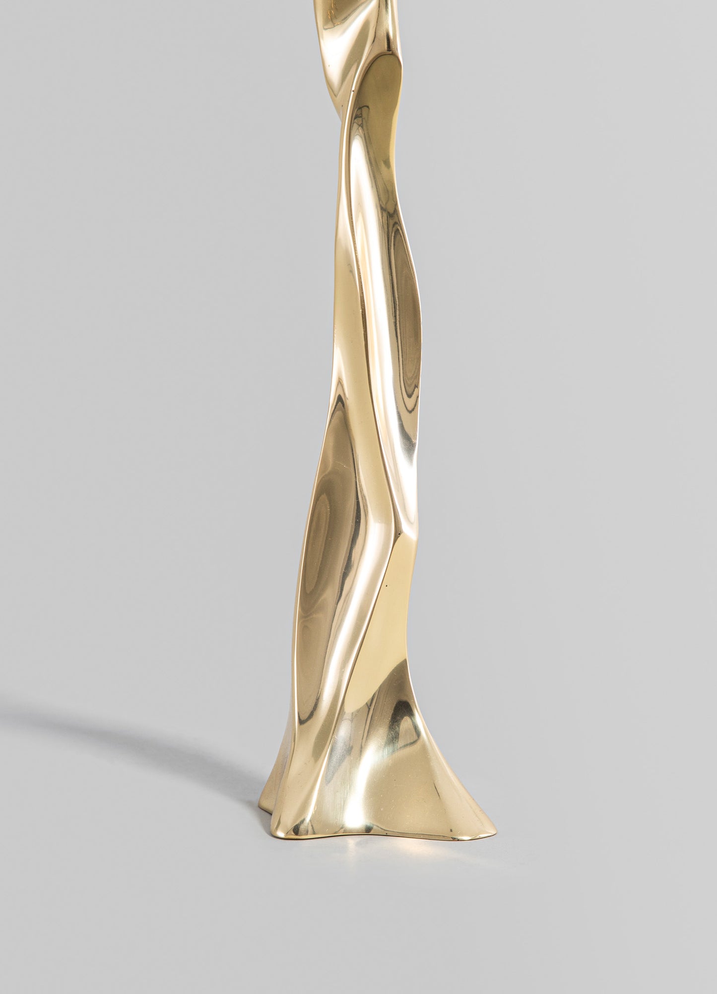 A sculptural table leg or decorative object made of polished brass with organic, flowing curves and a reflective metallic finish, set against a neutral background.
