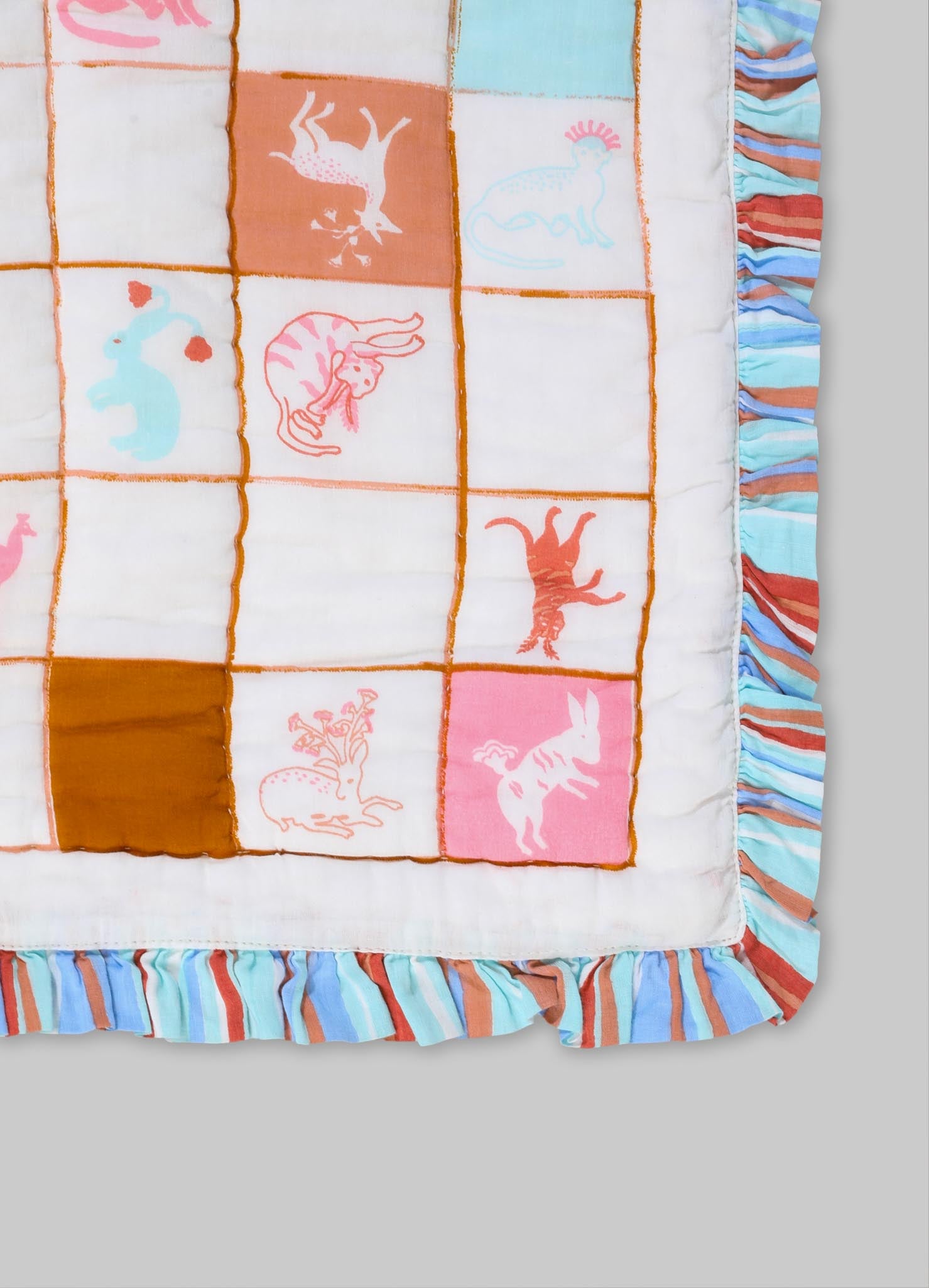 A cotton quilt with a patchwork design featuring animal motifs in pastel pink, orange, blue, and white. The quilt has a ruffled border with multicolored stripes in shades of blue, red, and beige.