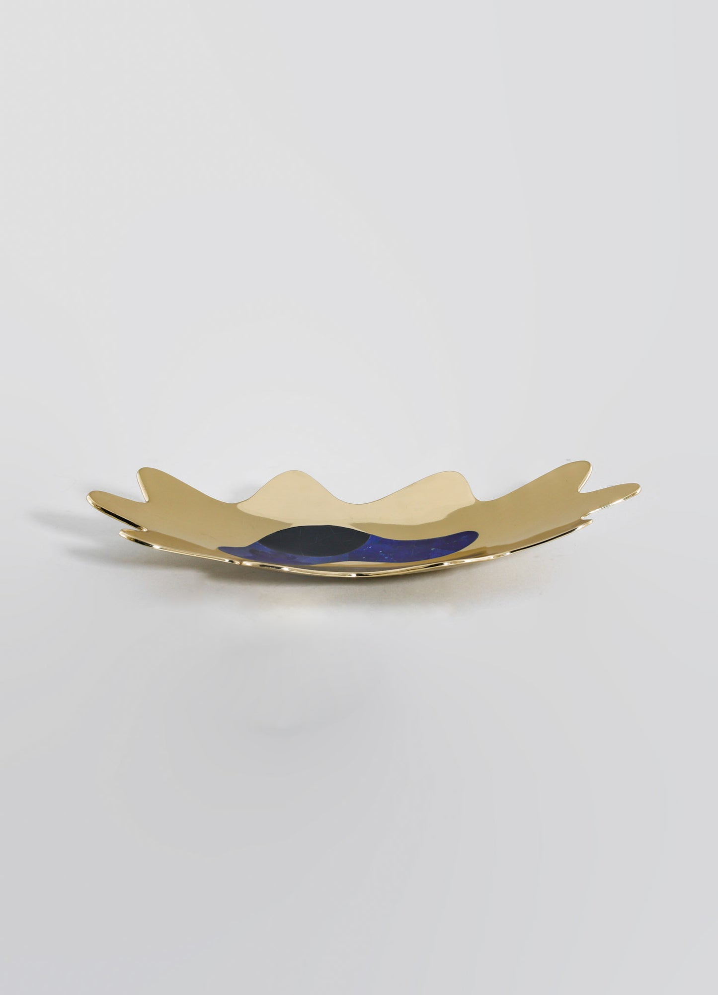 A decorative porcelain dish with an asymmetrical, organic shape featuring a gold and navy blue abstract design, placed on a plain background.