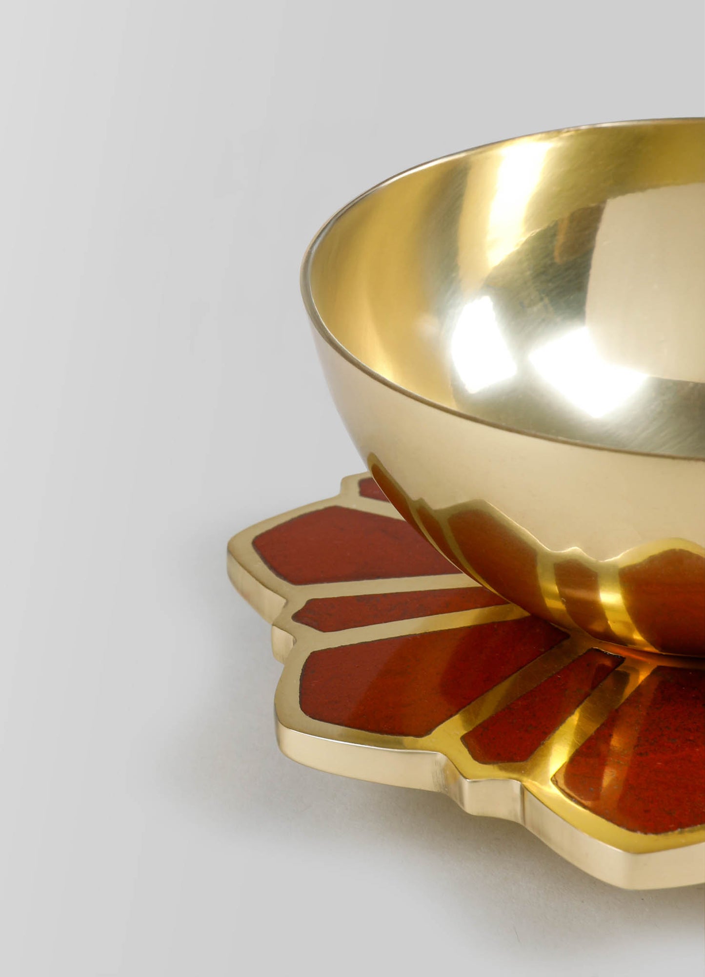 A gold-colored metal bowl with a smooth, reflective surface, placed on a decorative tray with red and beige petal-shaped segments.