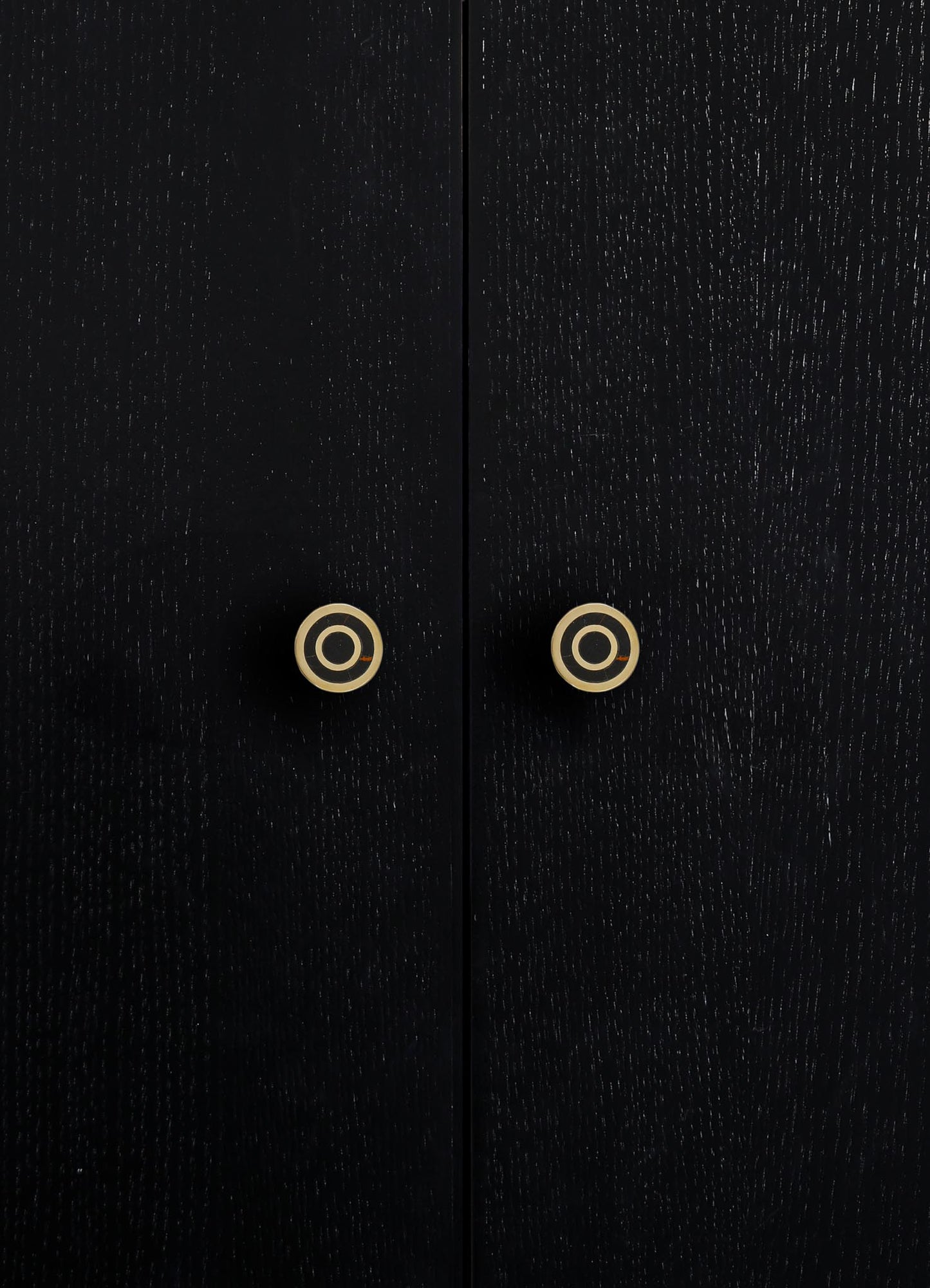 Close-up of black wooden furniture with a textured finish and round brass or gold-colored handles. The style appears contemporary with a focus on minimalistic design and metallic accents.