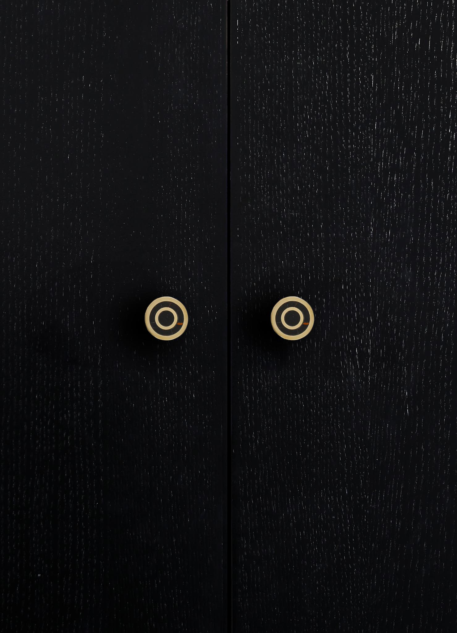 Close-up of black wooden furniture with a textured finish and round brass or gold-colored handles. The style appears contemporary with a focus on minimalistic design and metallic accents.