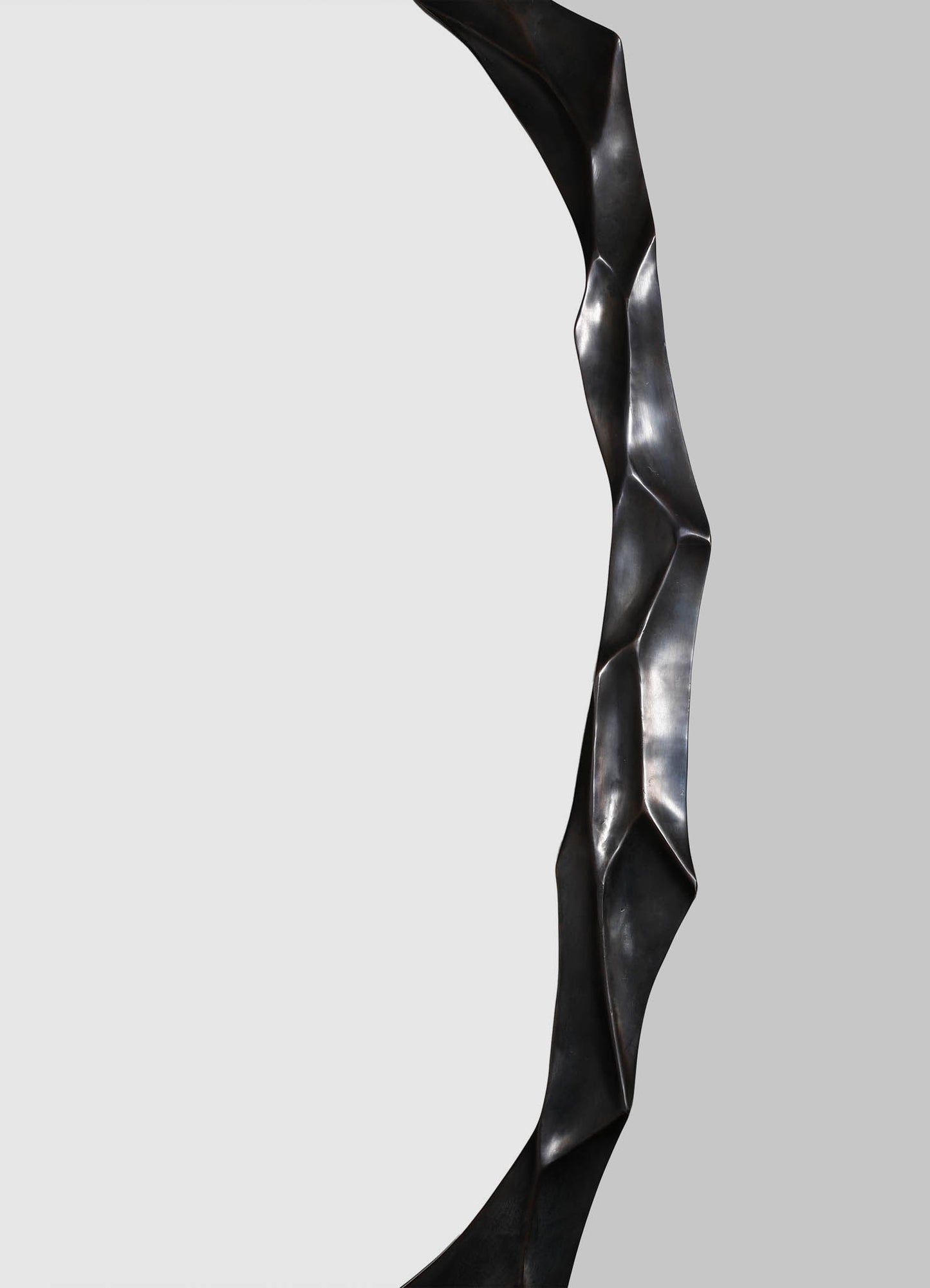 A close-up of a black metal sculpture with a twisted, organic form and a smooth, matte finish, set against a neutral grey background.