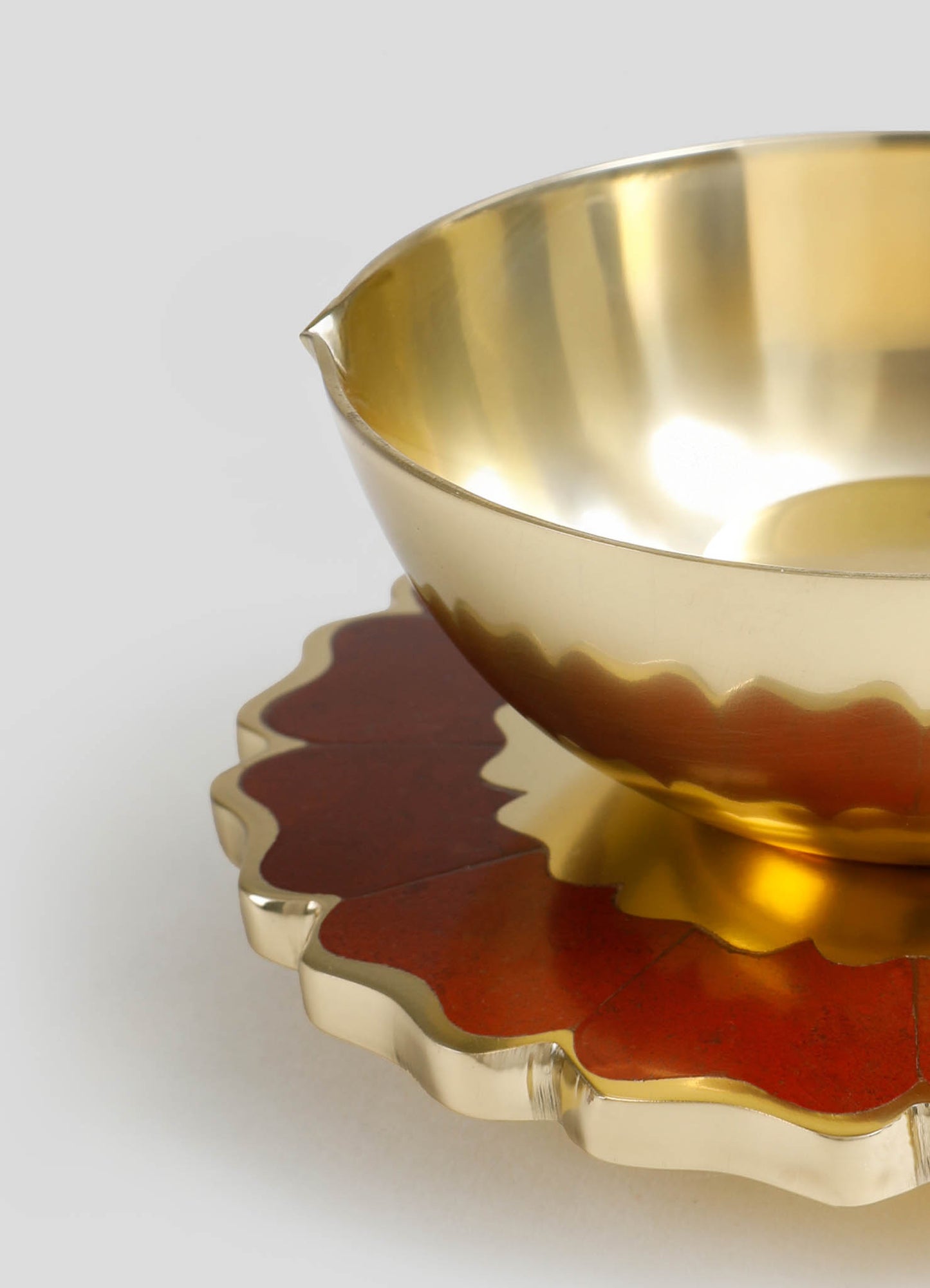 Gold-toned metal bowl with a smooth, reflective surface and a rounded shape, placed on a matching scalloped-edge tray with a red and gold finish, featuring a floral motif.