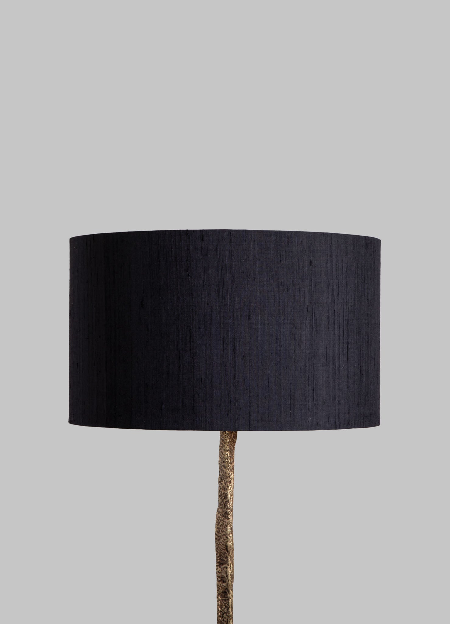 A floor lamp with a cylindrical black fabric lampshade and a textured gold-colored metal stand, set against a plain light gray background.