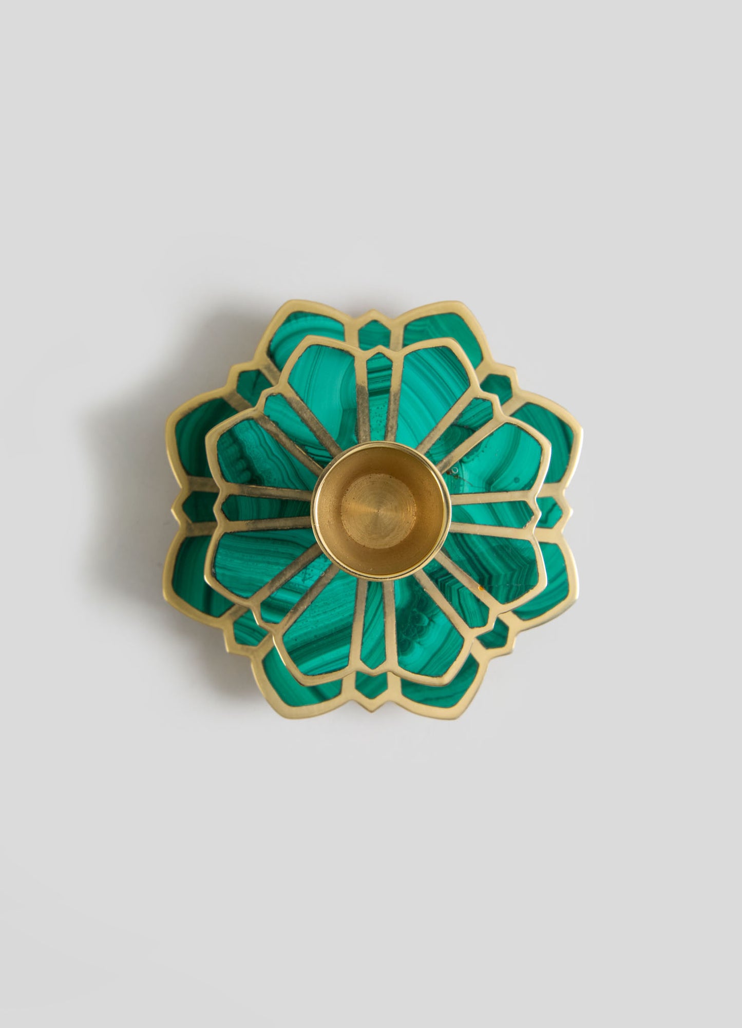 A decorative brass and malachite-colored glass candle holder with a layered, floral-inspired design featuring a central brass cup and geometric petal motifs.