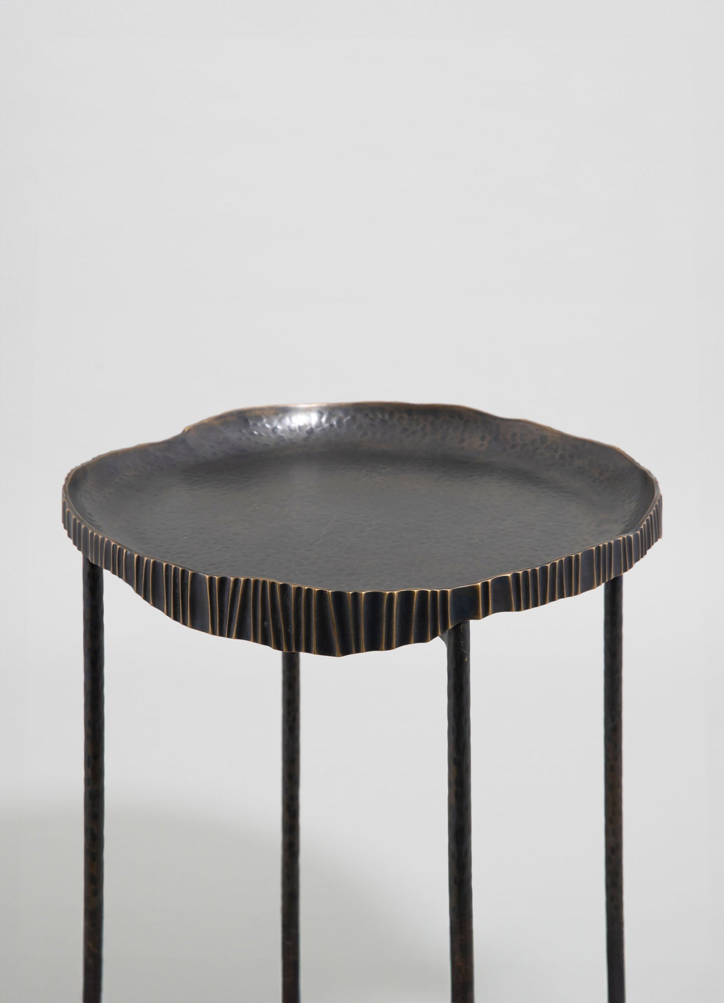 A small side table with a textured, irregularly shaped black top featuring subtle metallic accents, supported by four slender black metal legs.
