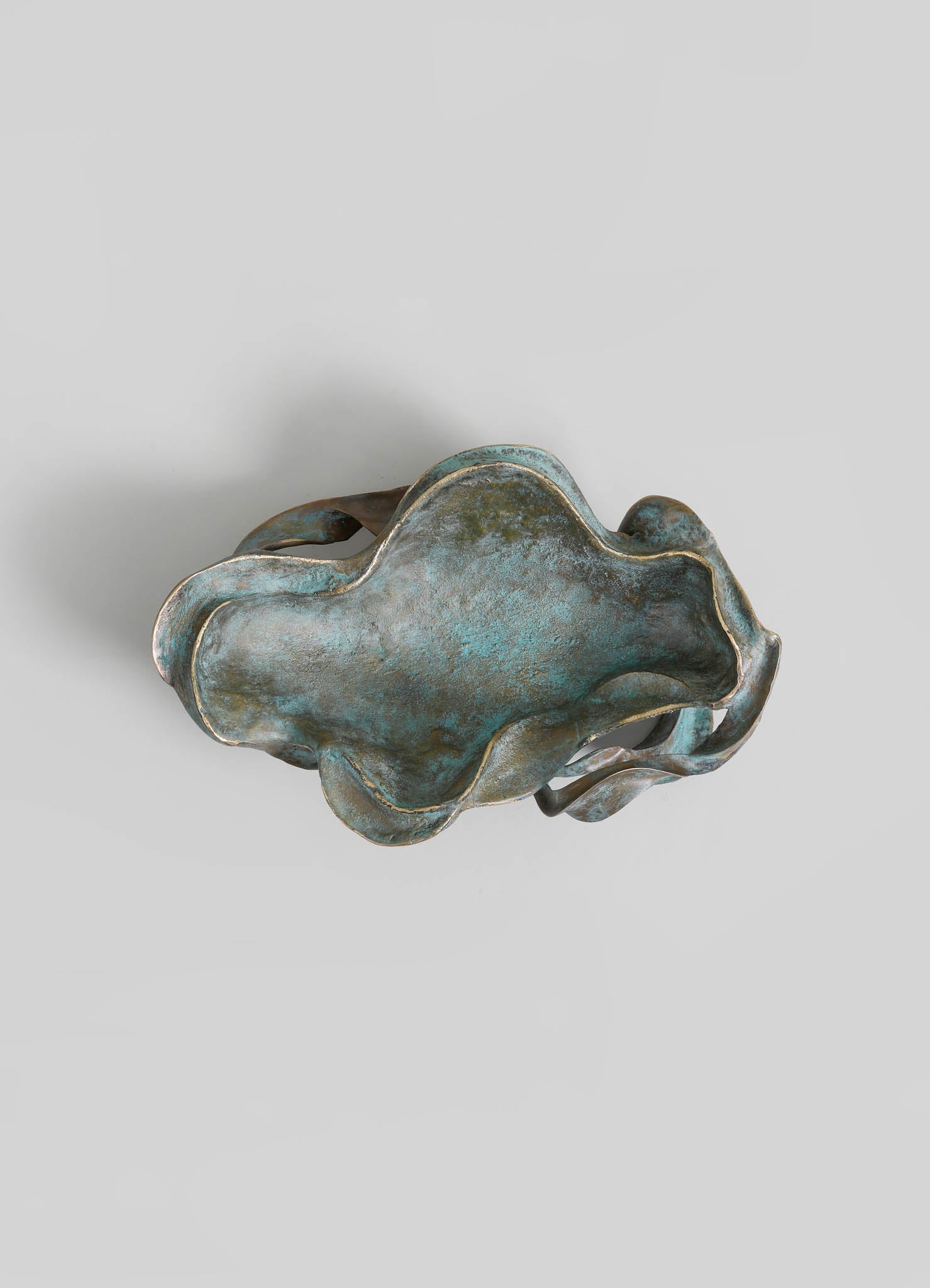 A decorative metal bowl with an organic, irregular shape and a patinated finish in shades of blue and bronze, featuring a textured, weathered surface.