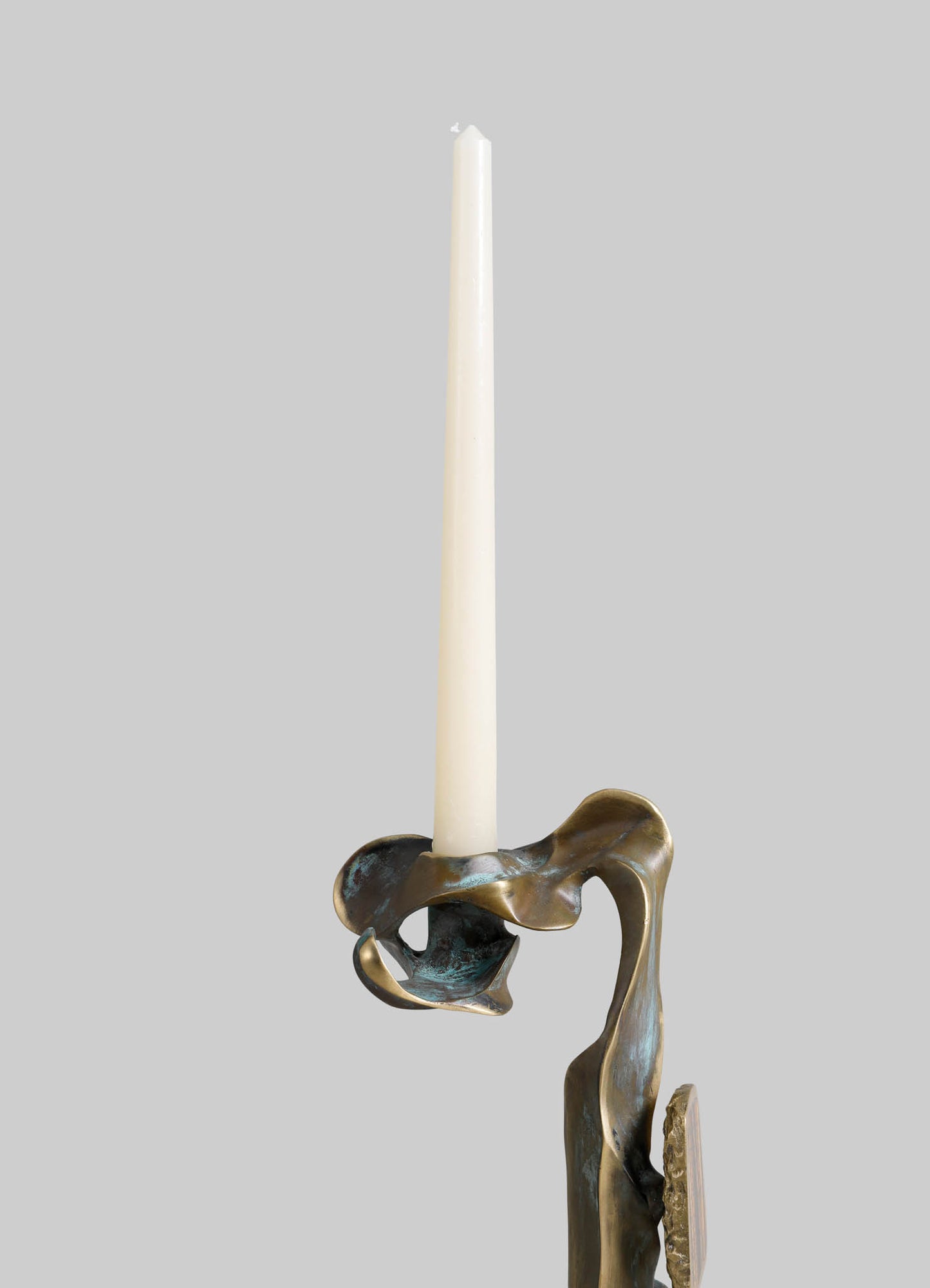 Brass candle holder with an abstract, flowing design and a metallic finish, holding a tall white taper candle.