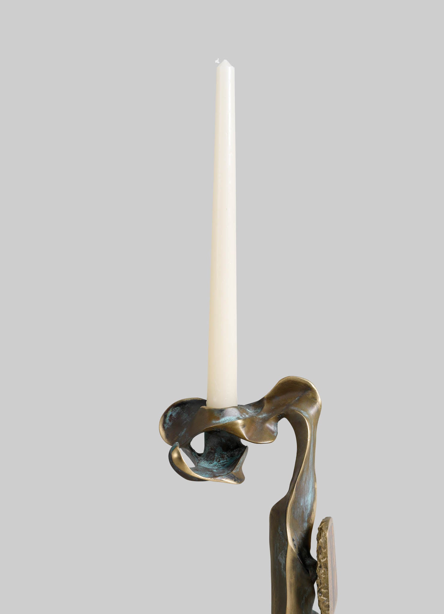 Brass candle holder with an abstract, flowing design and a metallic finish, holding a tall white taper candle.