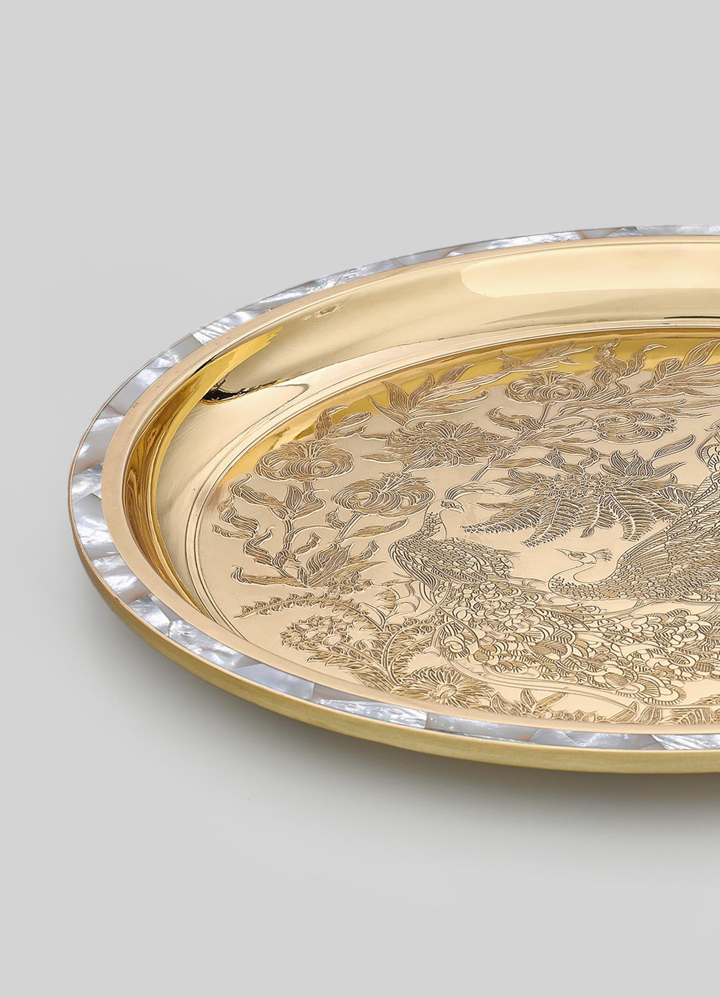 A decorative serving tray with a gold-tone metal surface engraved with intricate floral and bird motifs, edged with a clear acrylic or glass border. The tray combines elegant craftsmanship with a luxurious style.