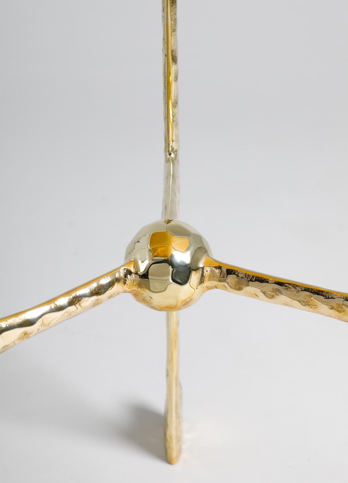 A decorative object made of polished brass with a spherical central element and three extending arms, featuring a shiny gold finish and a minimalist design.