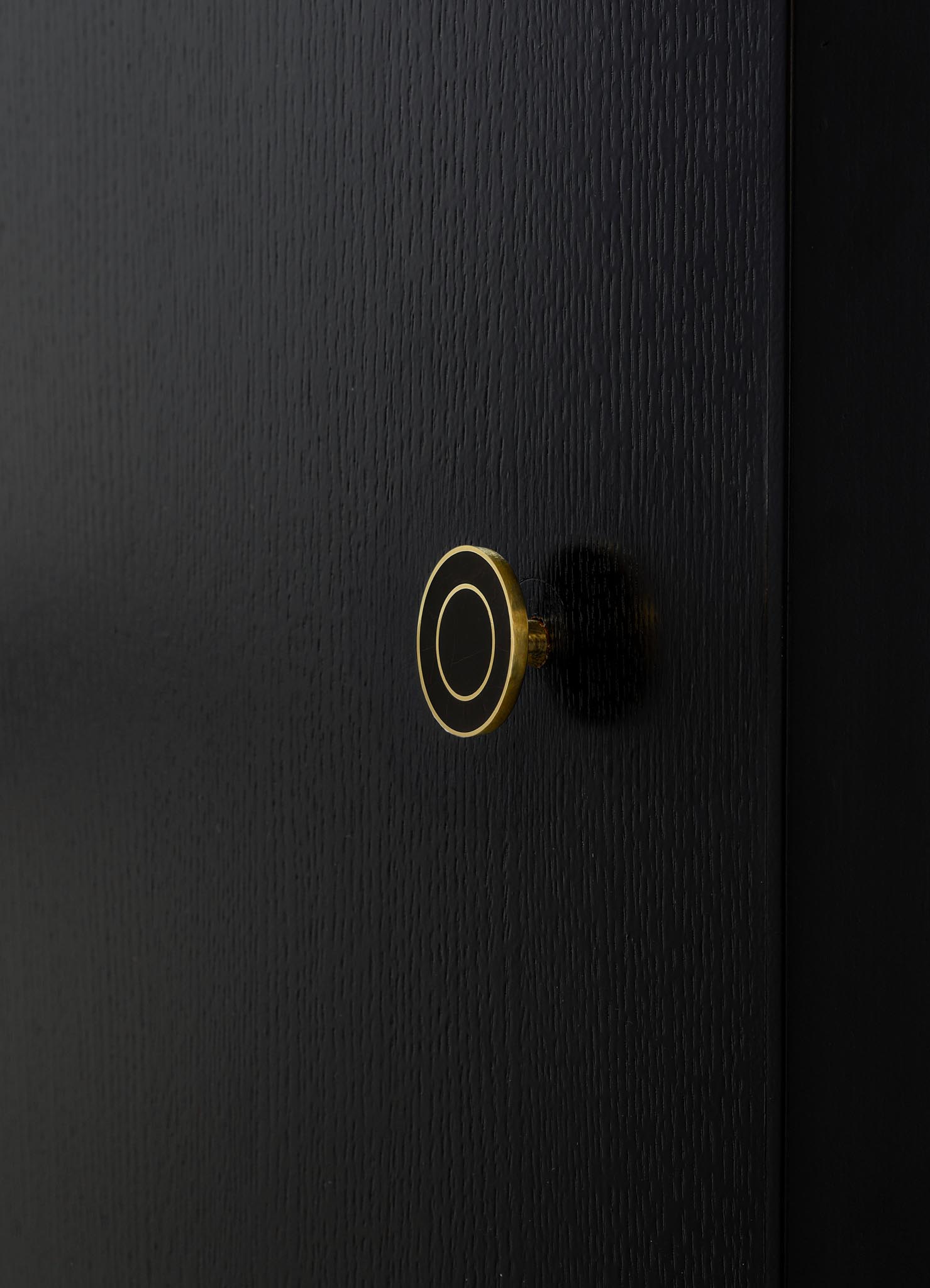 Close-up of a black wooden door featuring a round, metallic gold doorknob with black details. The door has a textured finish, emphasizing a sleek and modern style.
