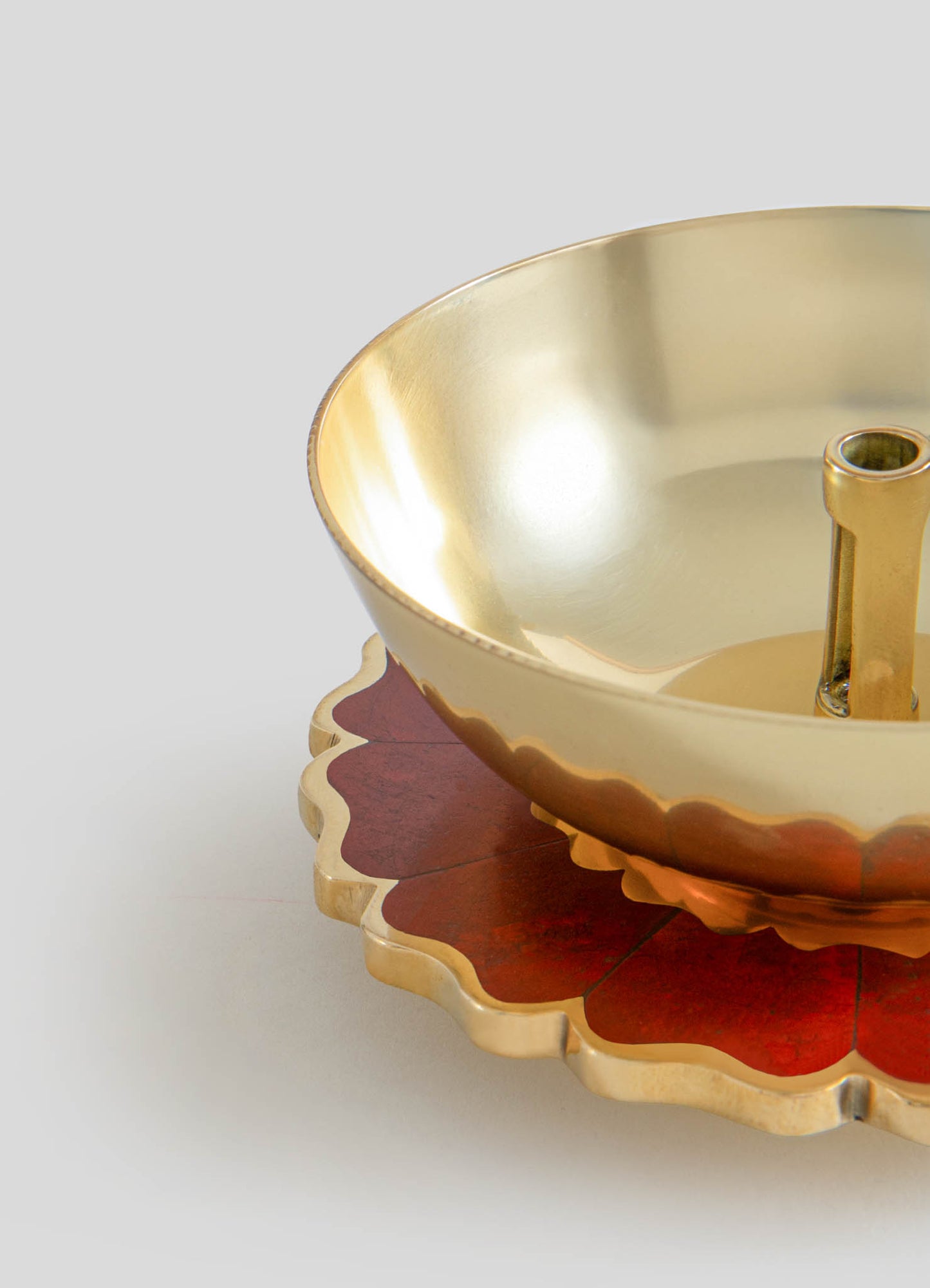 A brass bowl with a smooth, polished interior and a scalloped edge design, placed on a decorative wooden tray with a red and beige leaf motif.