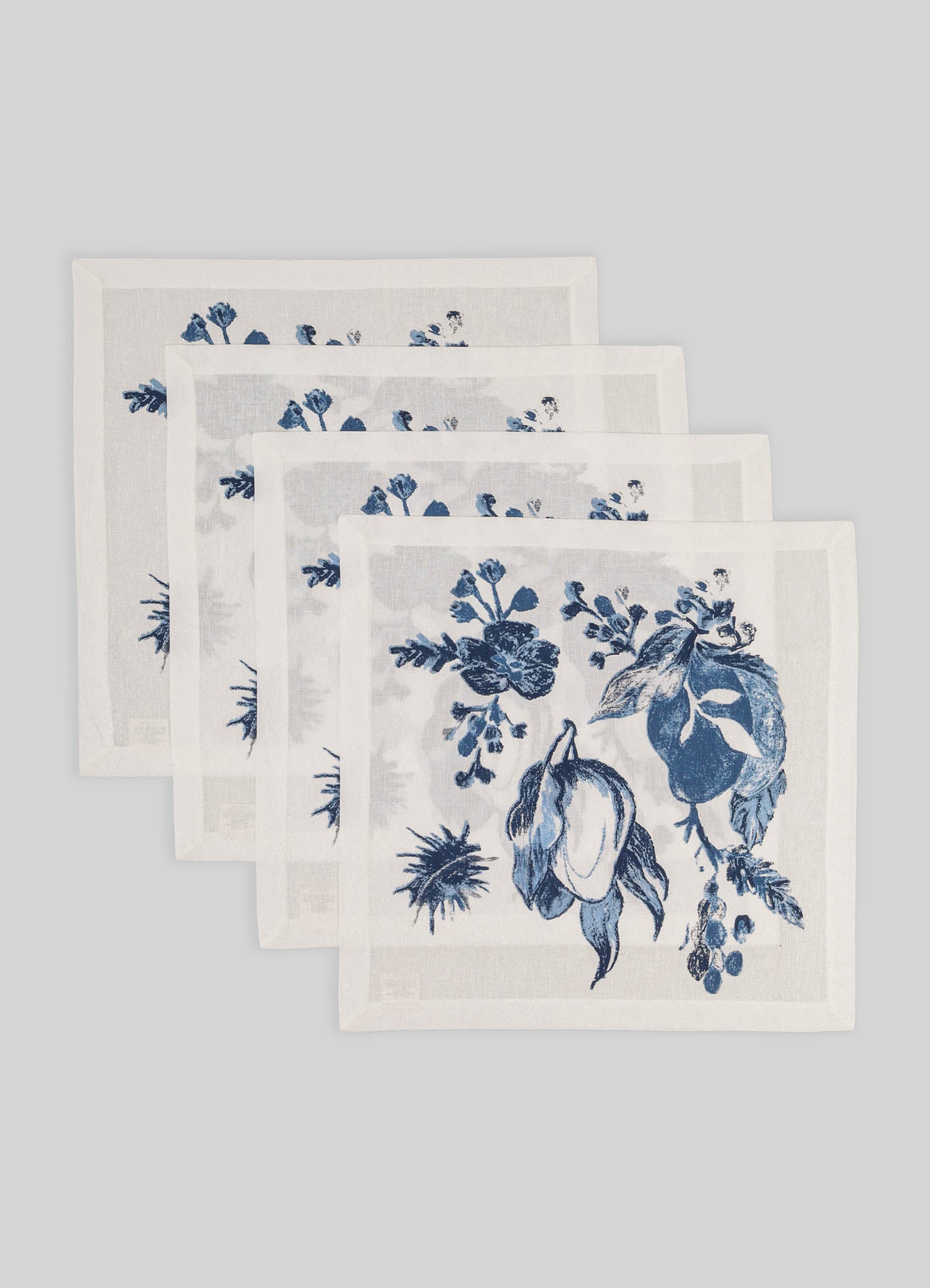 Set of five white linen napkins with blue floral prints, featuring botanical motifs and a delicate border, arranged on a light gray background.