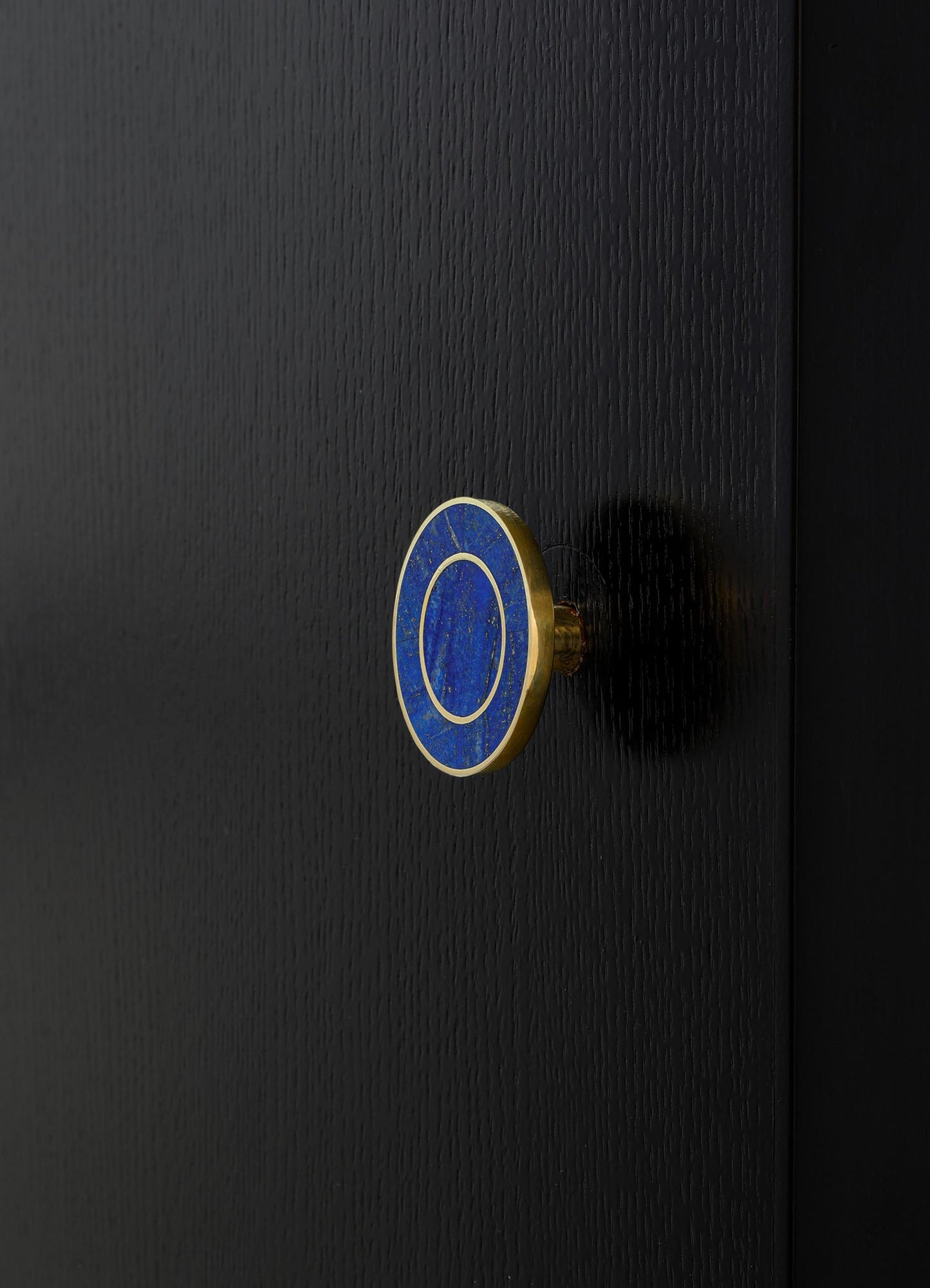 A close-up of a black textured surface with a round, blue and gold ceramic drawer knob featuring a circular pattern, set against a dark background.