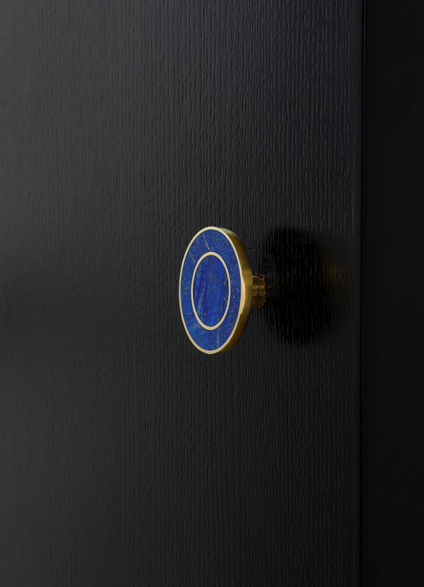A close-up of a black textured surface with a round, blue and gold ceramic drawer knob featuring a circular pattern, set against a dark background.