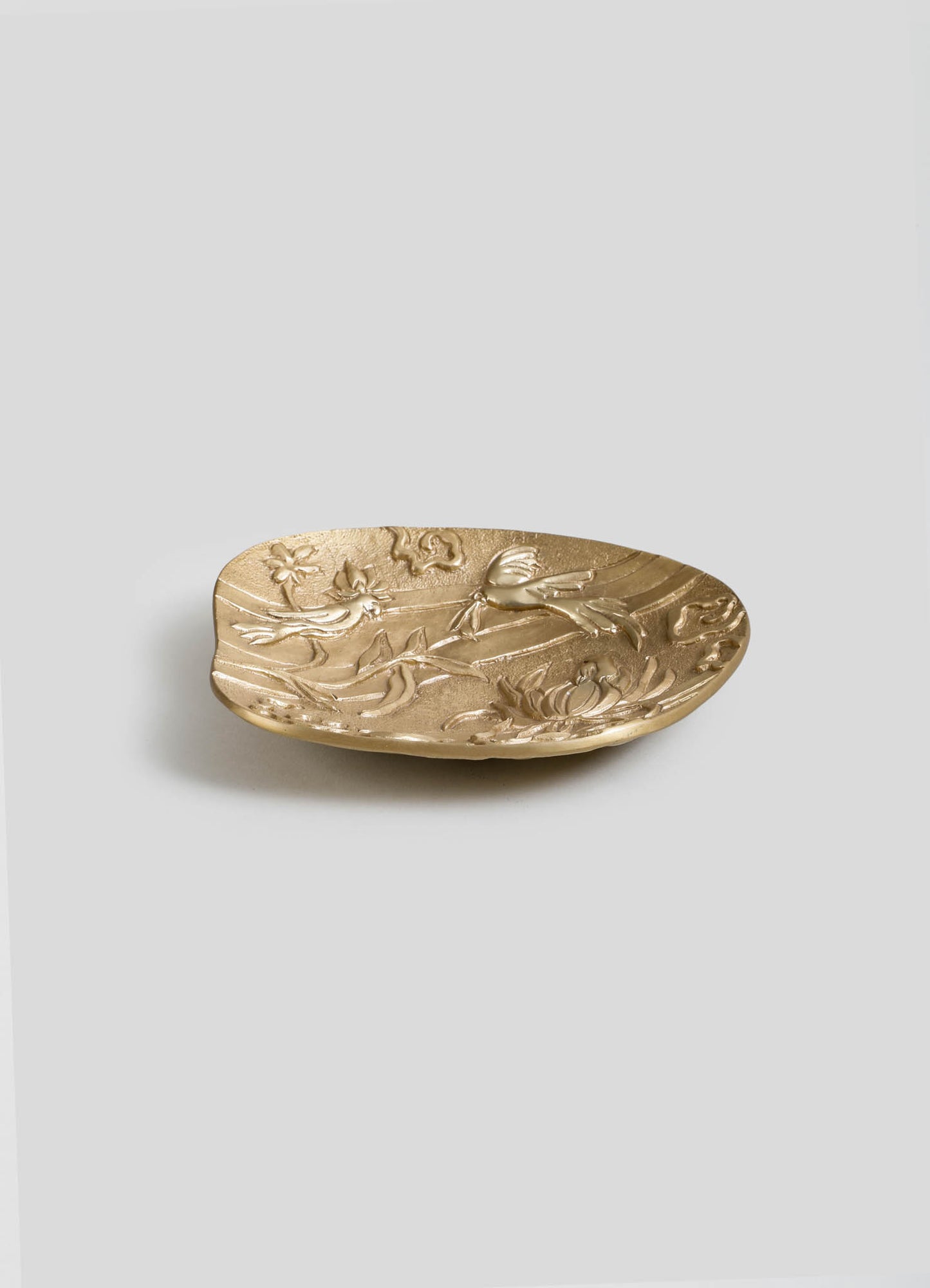 A brass dish with embossed floral and bird motifs, featuring a smooth, rounded shape and a metallic gold finish.