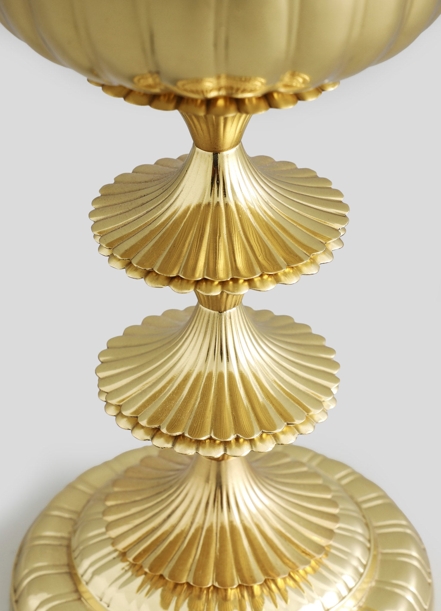 Gold-toned metal stand with scalloped, fluted surfaces arranged in three tiers, featuring a smooth, reflective finish. The design has a luxurious, vintage-inspired style with a detailed, textured motif.