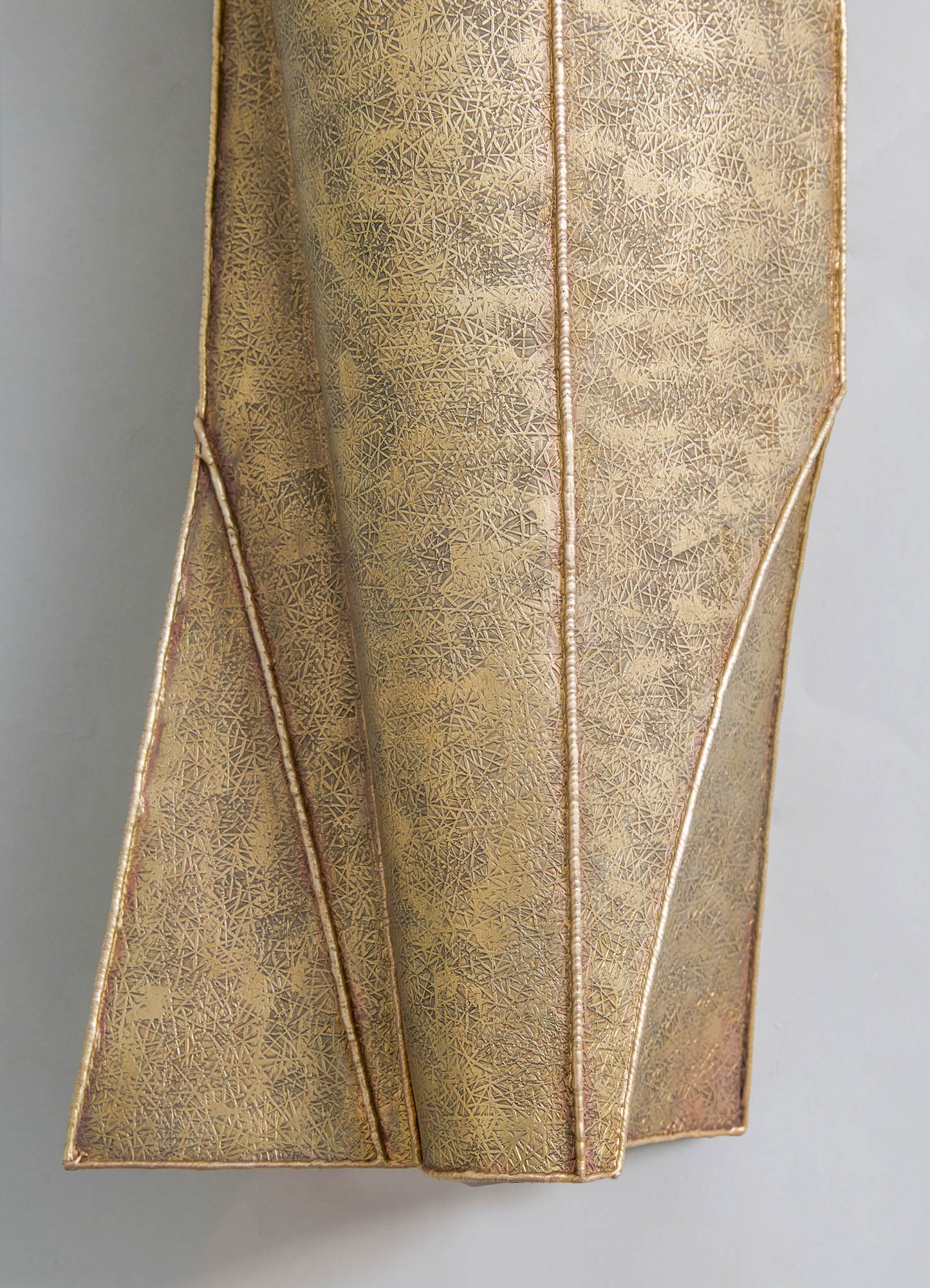 A decorative gold metal vase with intricate geometric engravings, featuring a tapered rectangular shape and clean, angular lines.