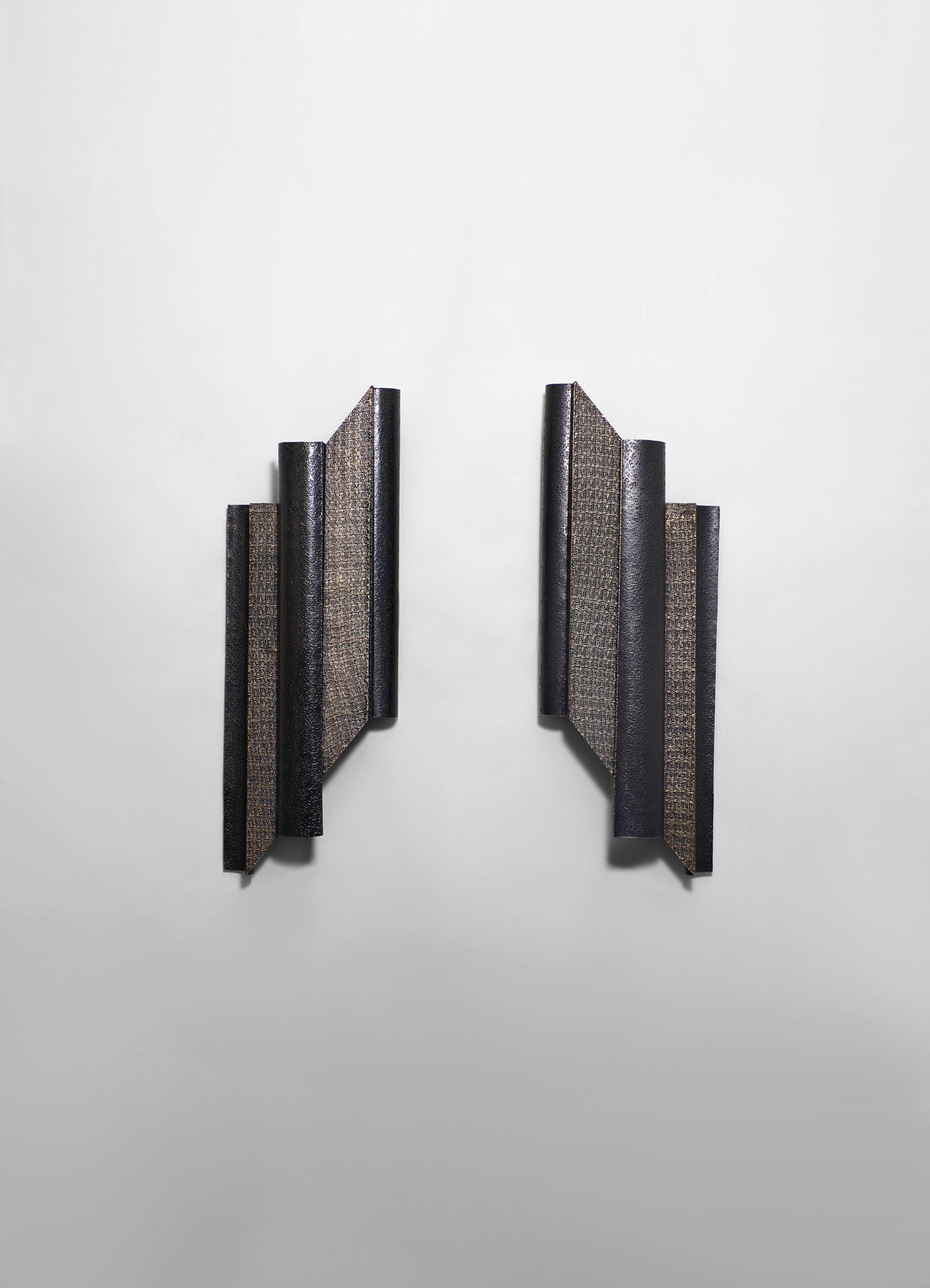 Black textured wall-mounted sculpture with angular, layered panels in a modern, geometric style, set against a plain white background.