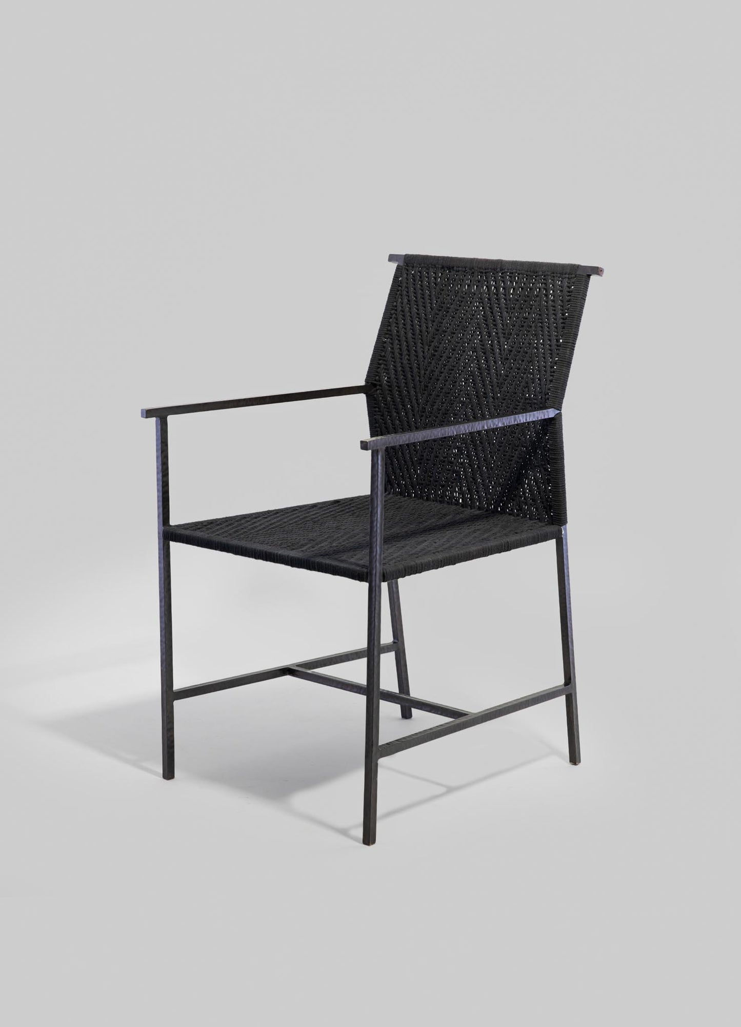 Black woven chair with a metal frame and armrests, featuring a textured geometric pattern on the backrest and seat, set against a plain background.