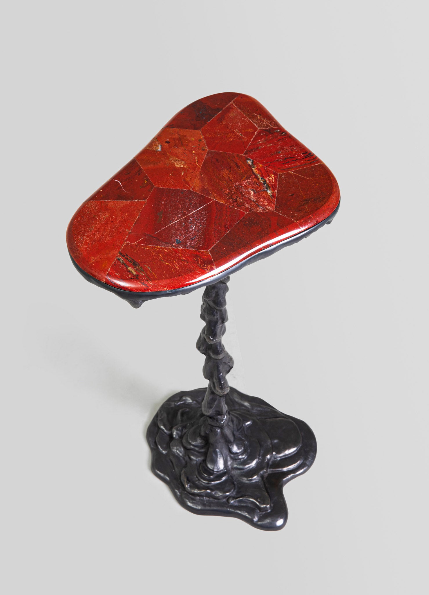 A small side table with a red, geometric patterned stone top and an irregular black metal base. The table combines natural stone and sculptural metal for an eclectic, artistic style.